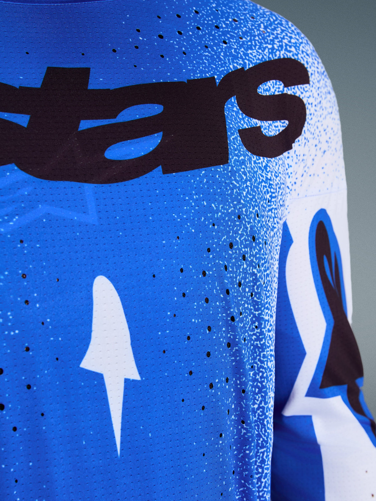 Alpinestars Supertech Scenz Jersey 2026, zbliżenie na niebiesko-biały design (Ucla Blue), laserowo wycinane perforacje dla lepszej wentylacji, czarny branding „stars” oraz oddychający materiał typu mesh do profesjonalnych wyścigów motocrossowych.