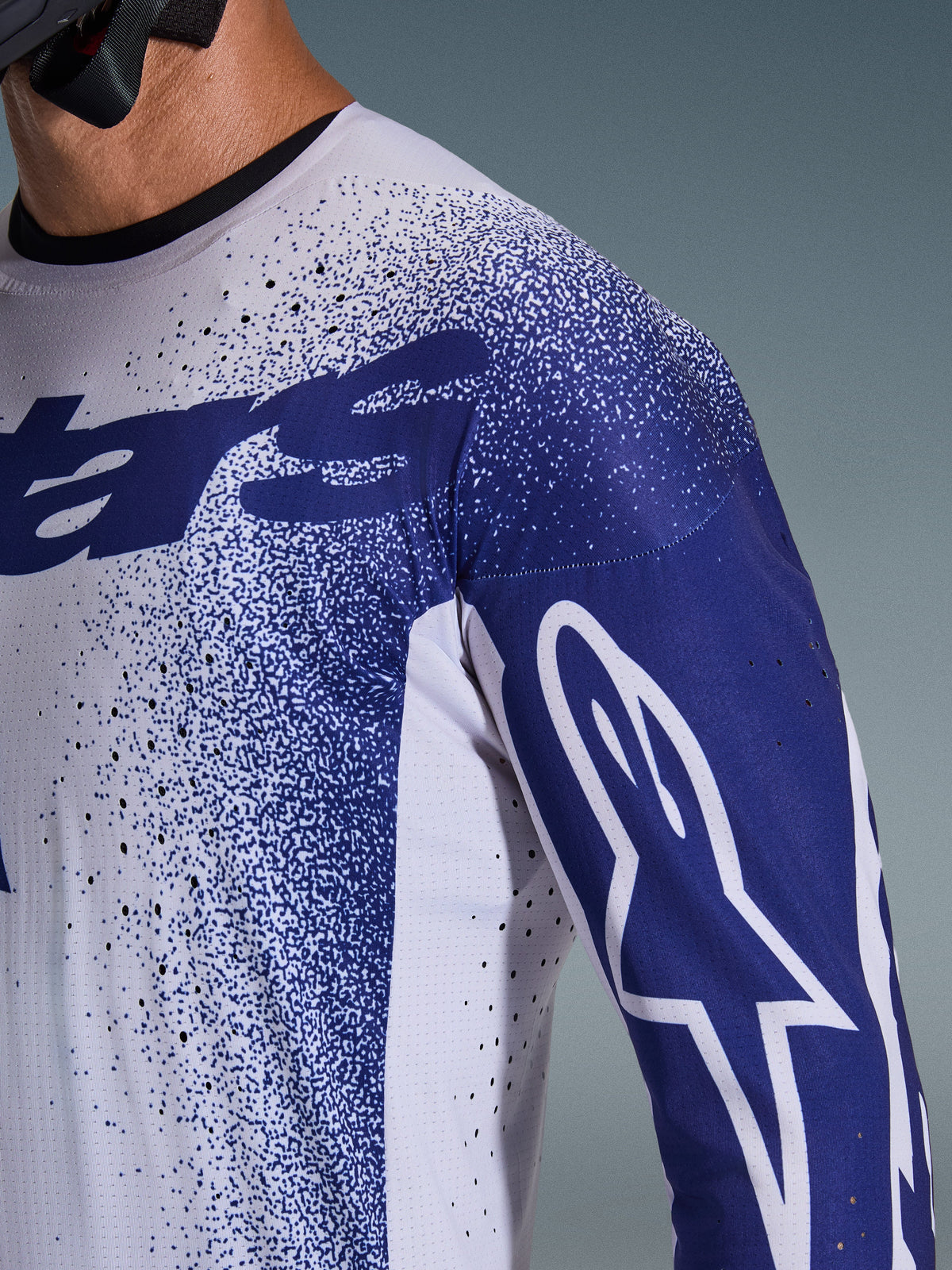 Alpinestars 2026 Supertech Scenz Jersey, zbliżenie na koszulkę w kolorze jasnoszarym i ciemnoniebieskim, laserowo wycinane perforacje, nakrapiany wzór graficzny, białe logo Astars na rękawie, profesjonalny krój motocrossowy