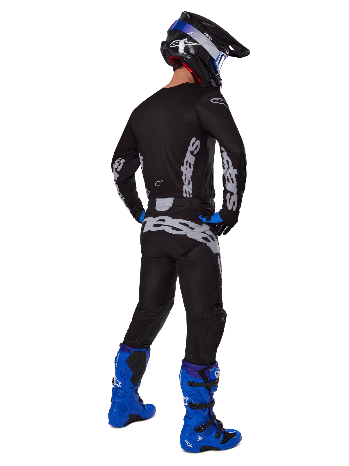 Motocrossista widziany z tyłu w zestawie Alpinestars 2025 Racer Graphite, czarno-szara koszulka i spodnie z szarym brandingiem, jasnoniebieskie buty motocrossowe, czarno-niebieski kask oraz niebieskie rękawice, kompletny strój off-road