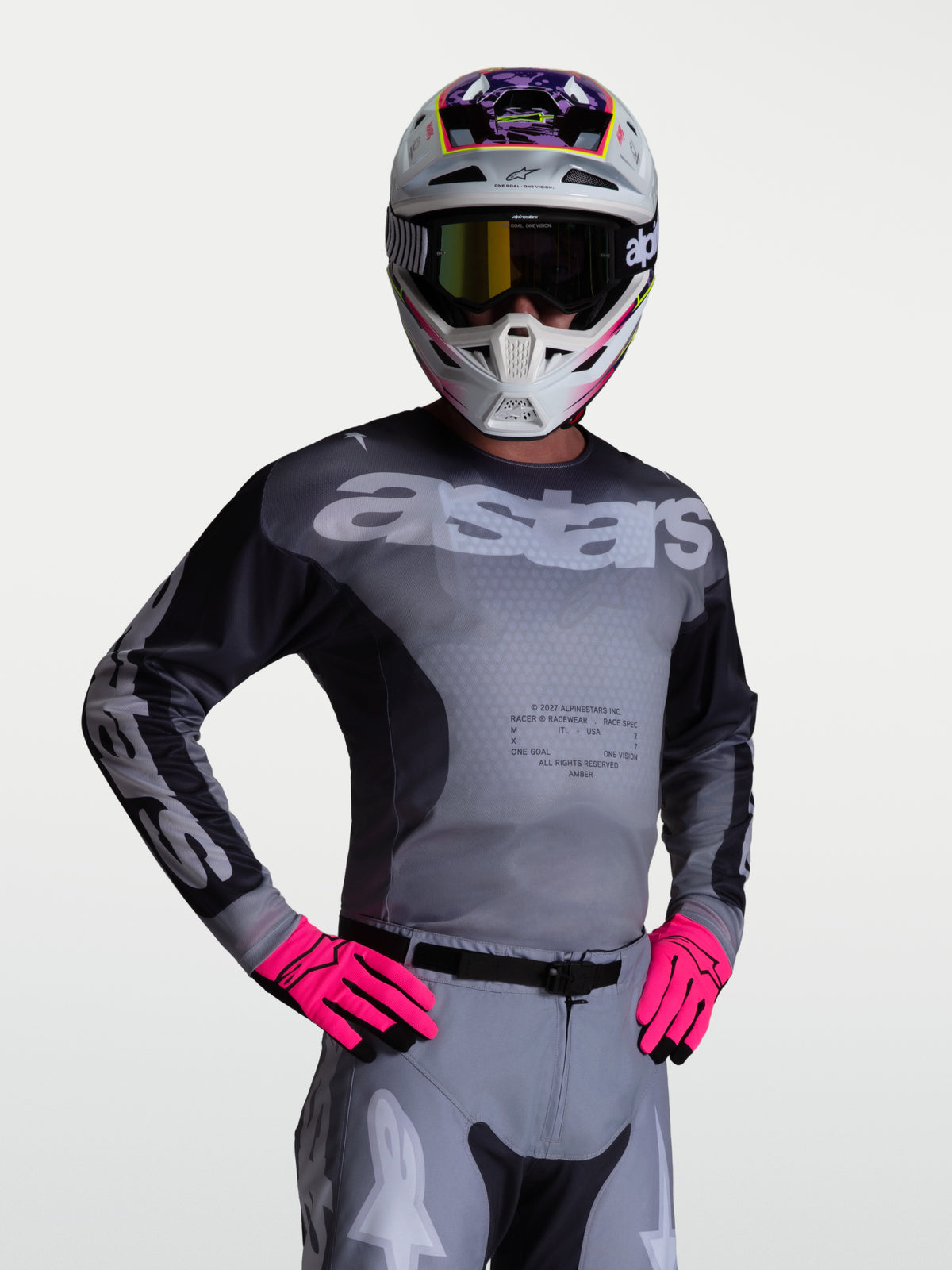 Alpinestars Koszulka Racer Amber, męska koszulka motocrossowa w kolorze szarym Graystone i jasnoliliowym Light Lilac, oddychające panele z siatki, widok na modelu w kasku i rękawicach.