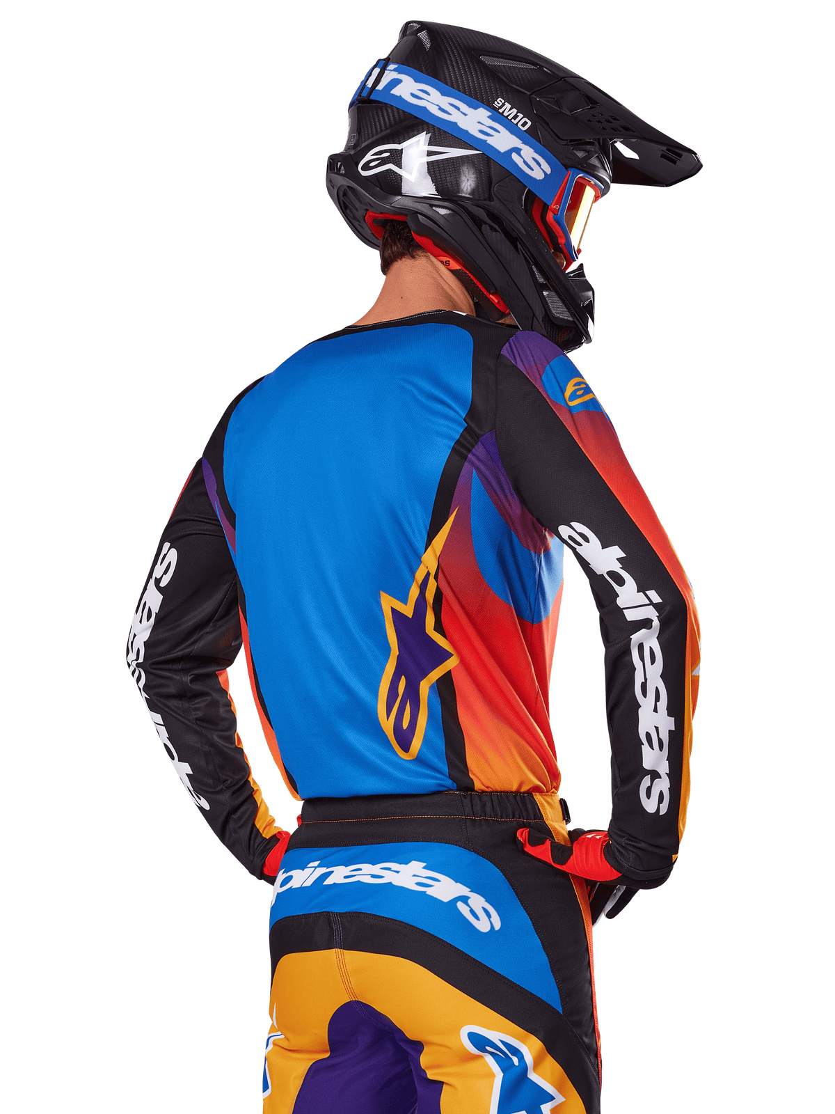 Motocrossowiec widziany od tyłu w zestawie Alpinestars 2025 Fluid Wurx, wielokolorowa koszulka z niebieskim tyłem i czarnymi rękawami z białym logo, pasujące pomarańczowo-niebieskie spodnie, czarno-niebieski kask z pomarańczowymi goglami, spójny strój do wyścigów terenowych.
