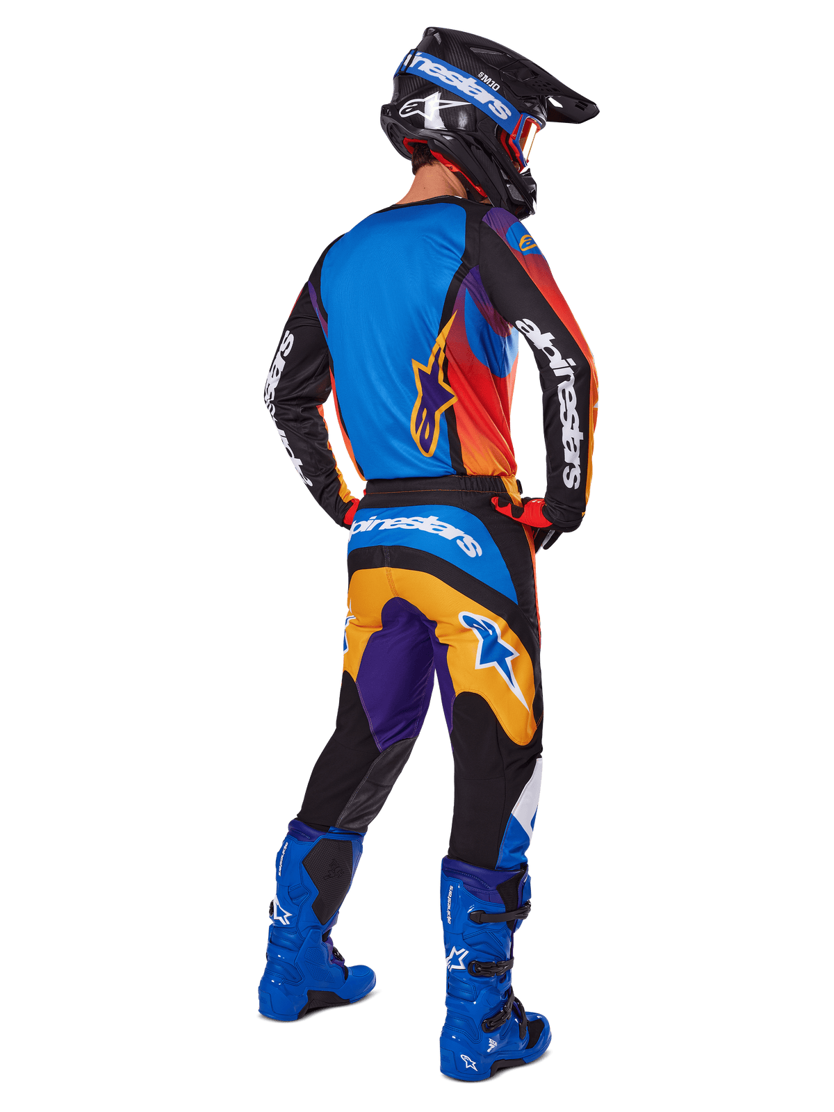 Motocyklista motocrossowy widziany od tyłu w zestawie Alpinestars 2025 Fluid Wurx, wielokolorowa koszulka z niebieskimi, pomarańczowymi i fioletowymi panelami, pasujące spodnie z białym logo Alpinestars na siedzeniu, jaskrawoniebieskie buty i czarny kask, skoordynowany strój do wyścigów terenowych