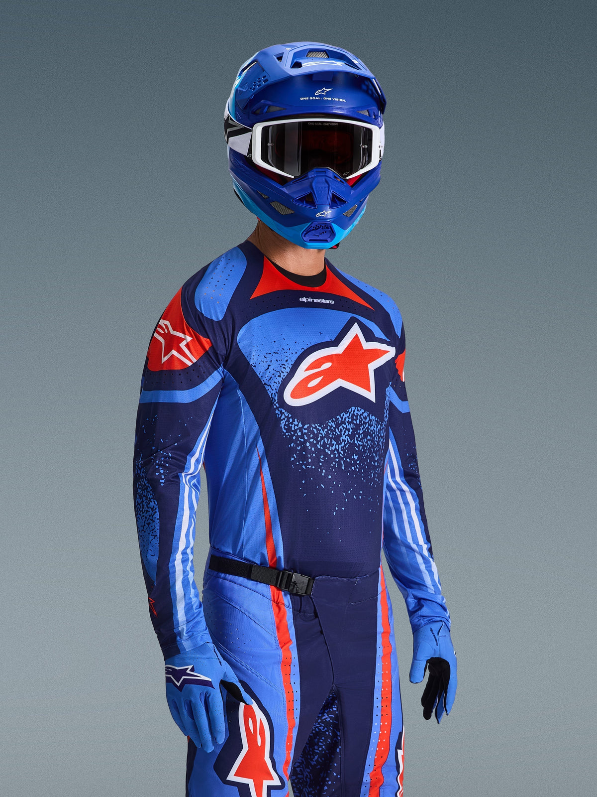 Zawodnik motocrossowy w koszulce Alpinestars 2026 Techstar Nomur, strój wyścigowy w barwach granatowo-pomarańczowych i błękitnych (UCLA Blue), z dużym pomarańczowym logo Astars, pasujący niebieski kask i rękawice, sportowy ubiór do zawodów terenowych