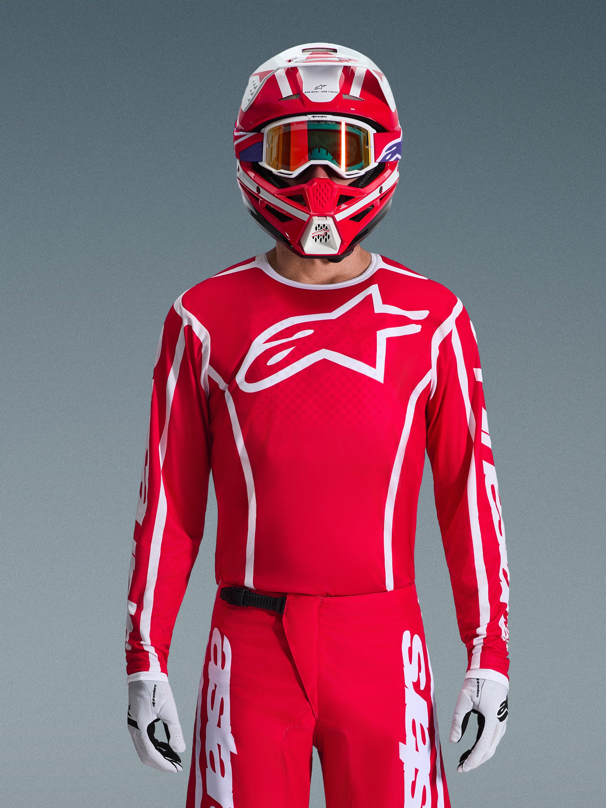 Zawodnik motocrossowy w kompletnym zestawie Alpinestars 2026 Fluid Apex, czerwona koszulka z dużym białym logo gwiazdy na piersi, pasujące czerwone spodnie z białym logowaniem, czerwono-biały kask z opalizującymi goglami, biało-czarne rękawice, dopasowany czerwono-biały strój do wyścigów terenowych