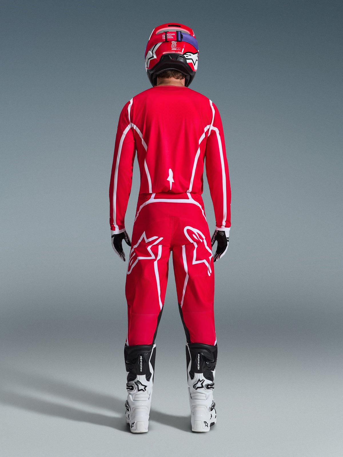 Widok z tyłu motocyklisty motocrossowego w zestawie Alpinestars 2026 Fluid Apex, jaskrawoczerwona koszulka i spodnie z białymi pasami i logo, biało-czarne buty i czerwony kask, profesjonalny strój do wyścigów terenowych
