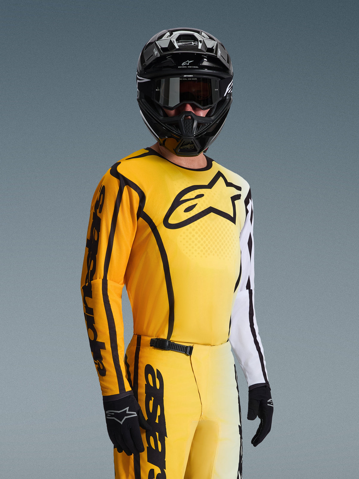 Motocross rider wearing the Alpinestars 2026 Fluid Apex Gear Set, yellow and white jersey with black star logo and accents, matching yellow pants, black helmet with black goggles, and black gloves, coordinated outfit for off-road racing