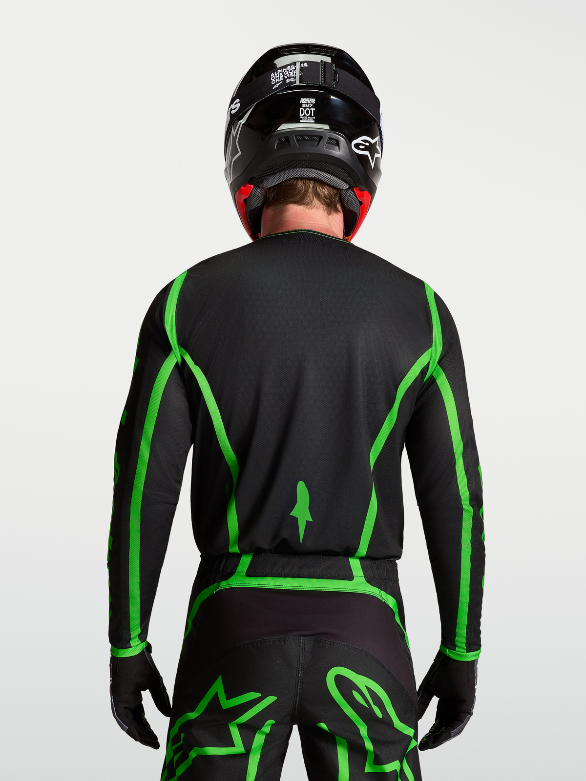 Alpinestars Fluid Apex V2, męska koszulka motocrossowa, czarna i jaskrawozielona, widok z tyłu na modelu ukazujący przedłużony krój pleców.