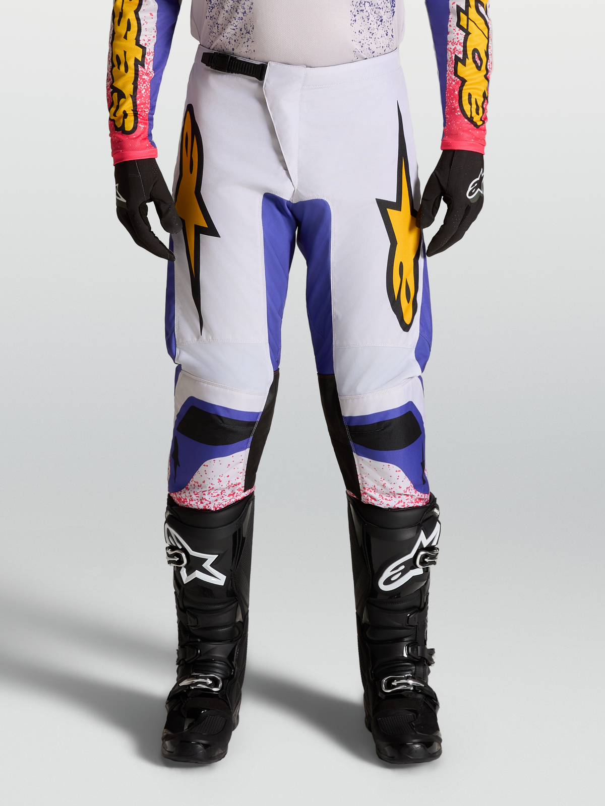 Alpinestars Spodnie Fluid Drag 2027, męskie spodnie motocrossowe na modelu, jasnoliliowe i niebieskie ze złotymi akcentami, sportowy krój do jazdy off-road