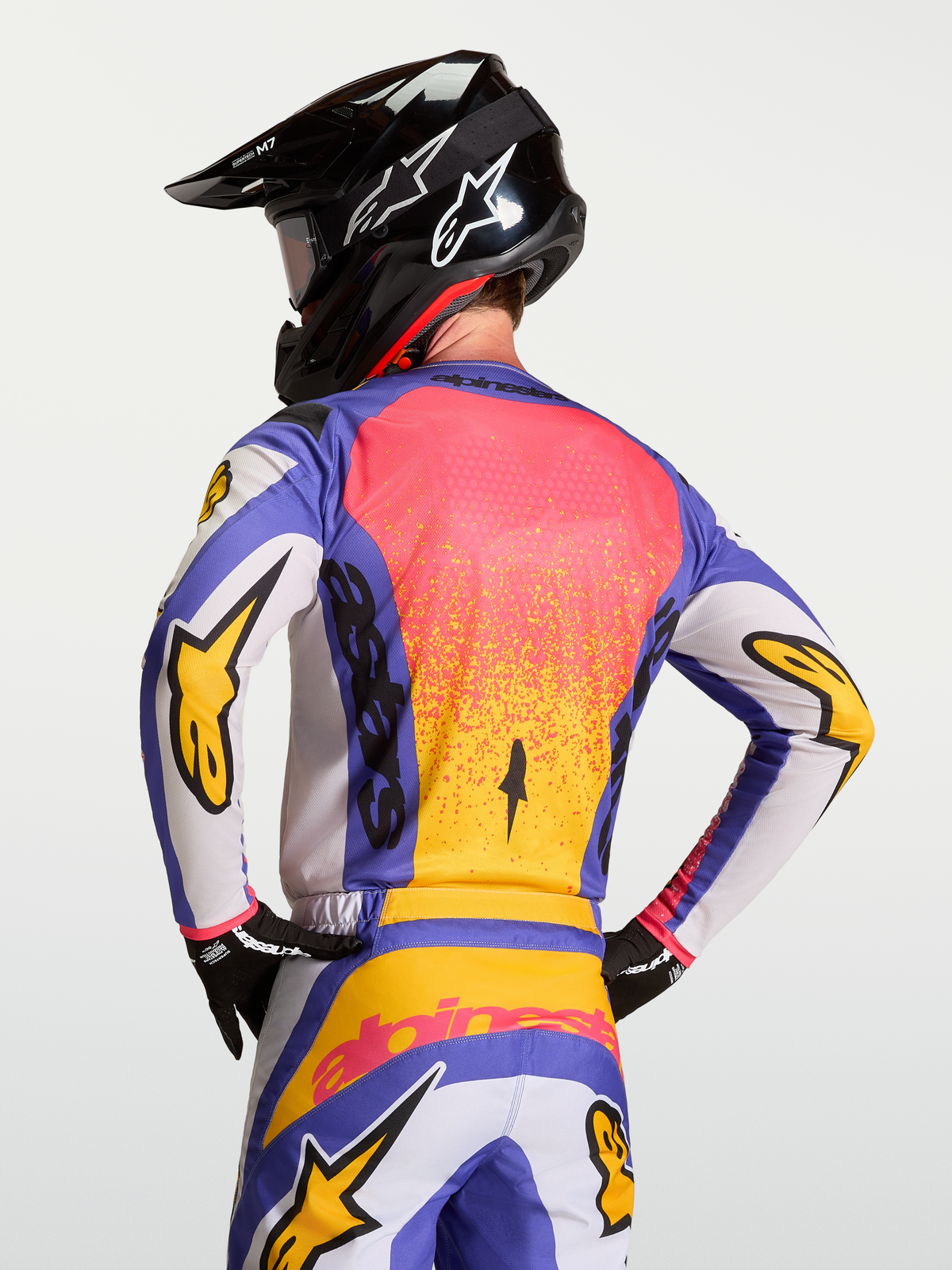 Alpinestars Koszulka Fluid Drag, niebieska i złota, męska koszulka motocrossowa z ergonomicznym tyłem, na modelu w kasku.