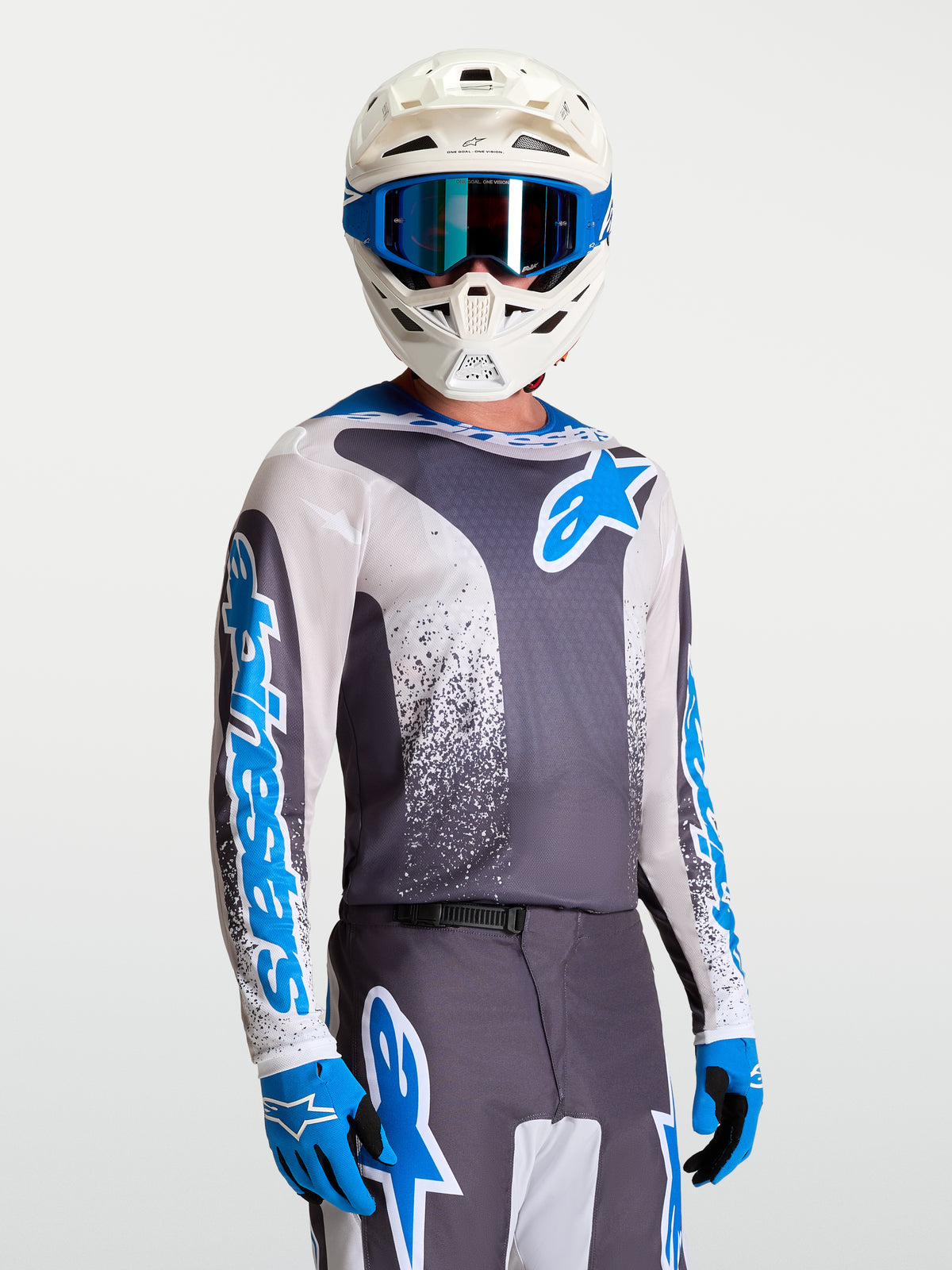 Alpinestars Koszulka Fluid Drag, wyczynowa koszulka motocrossowa, szara i niebieska, na modelu w białym kasku i rękawicach, lekki i oddychający materiał off-road