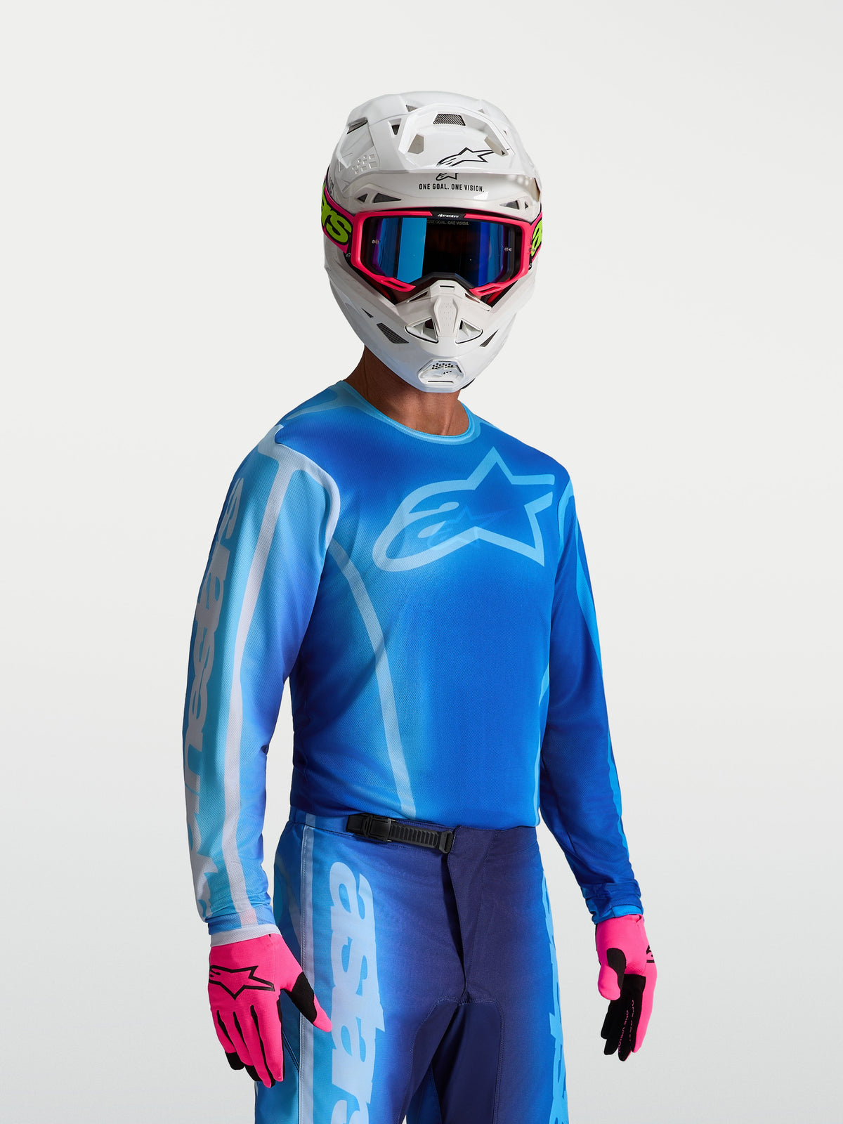Alpinestars Koszulka Fluid Kepler, męska koszulka motocrossowa wyścigowa, niebieska i jasnoniebieska, oddychający materiał odprowadzający wilgoć, model w białym kasku i różowych rękawicach.