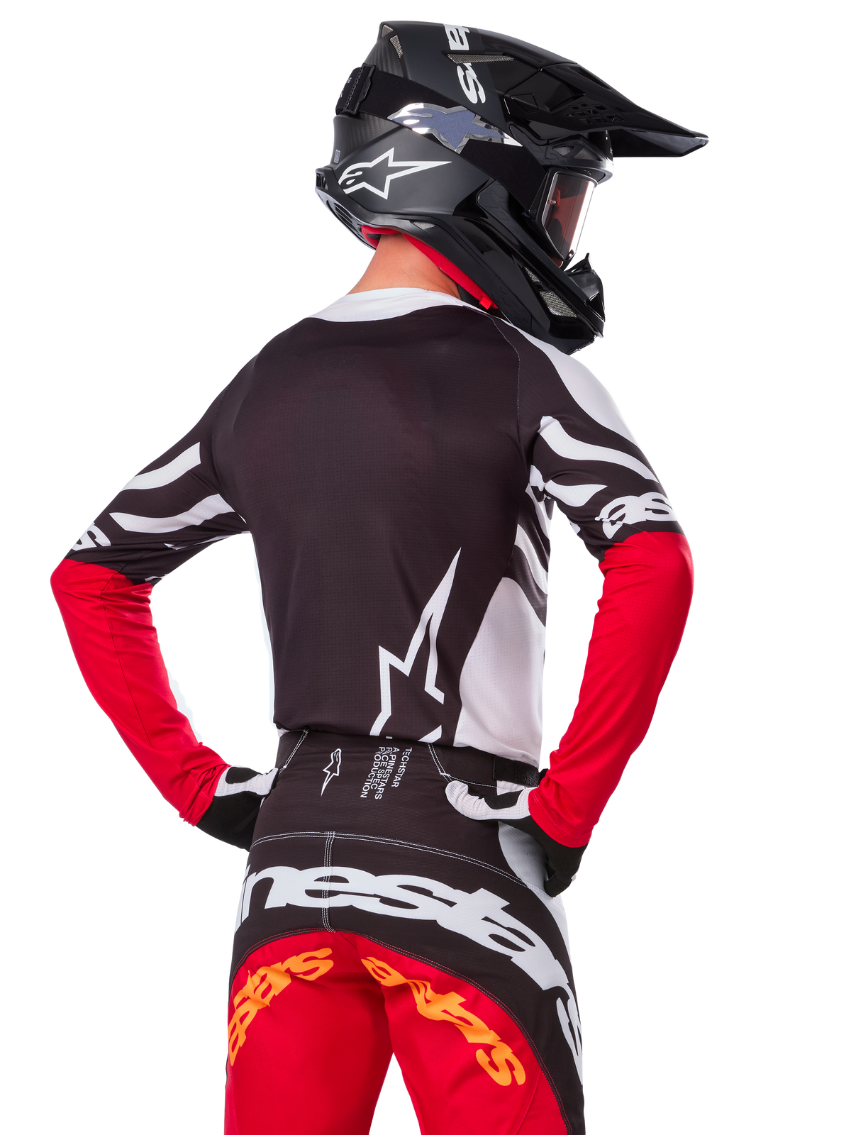 Motocross rider wearing complete racing gear, Alpinestars Limited Edition Techstar Deep Jersey in Black White and High Red, back view, matching Techstar Deep pants, black helmet with goggles, black and white gloves, professional off-road racing outfit