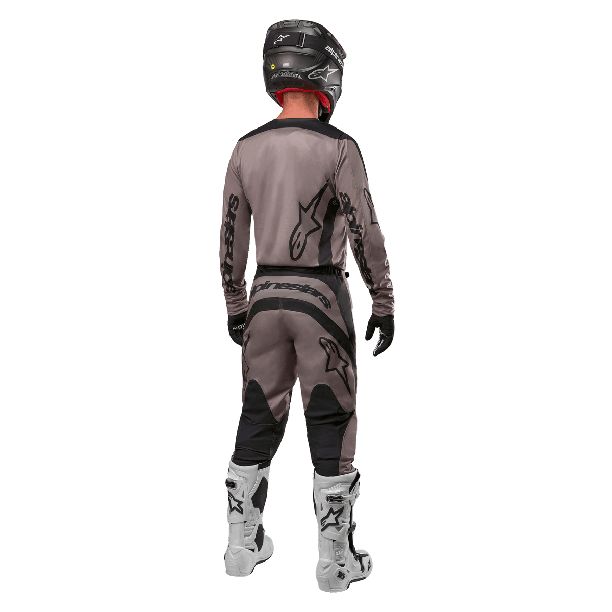 Alpinestars 2024 Fluid Lurv Jersey, koszulka motocrossowa, Mud Black, widok z tyłu zawodnika motocrossowego w dopasowanym stroju wyścigowym, czarny kask i białe buty, wyraźne czarne logotypy Alpinestars, sportowy krój zapewniający wydajność w terenie