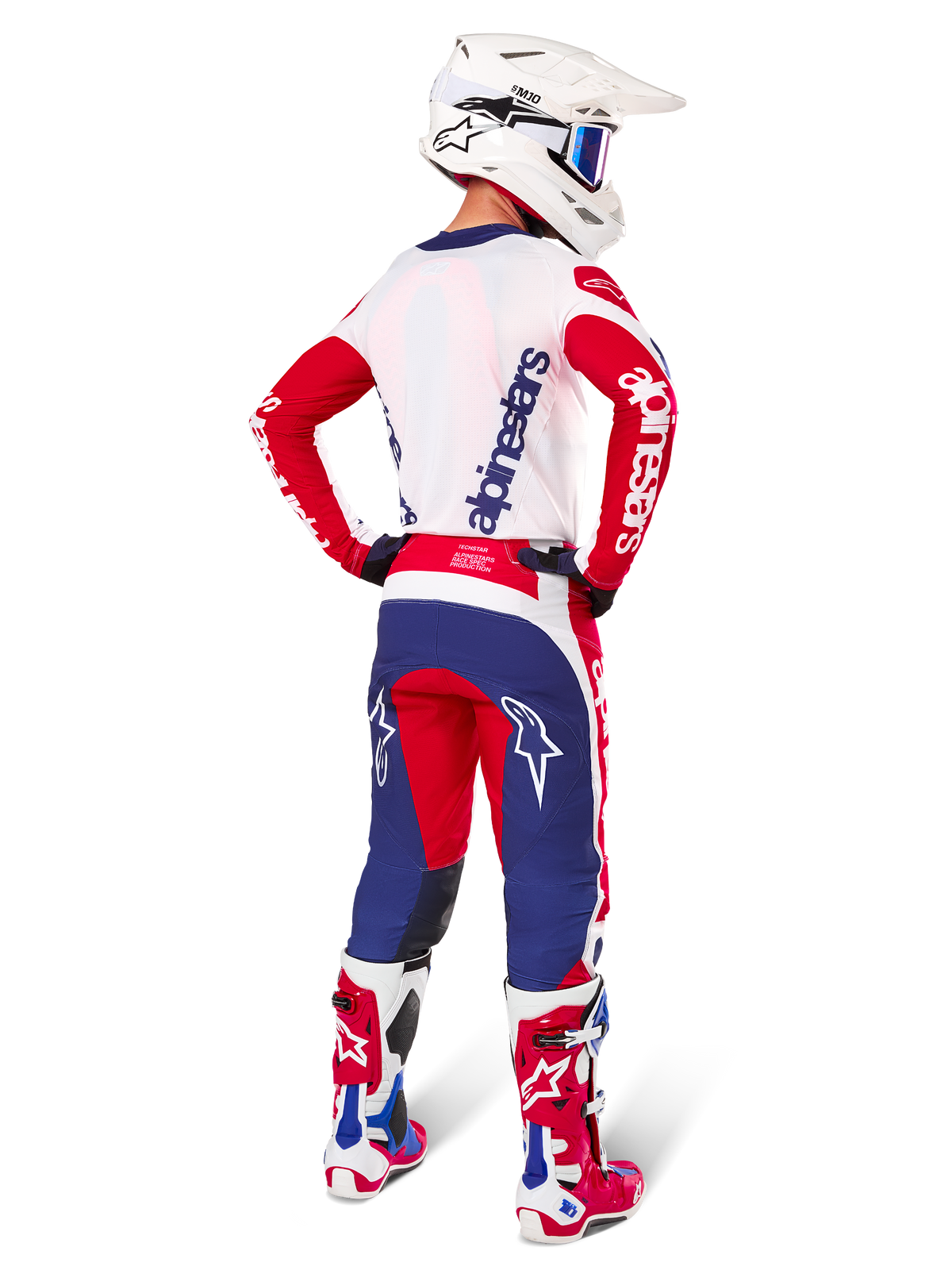 Zawodnik motocrossowy widziany od tyłu w zestawie Alpinestars Limited Edition Techstar Fortitude, kolorystyka Bright Red White and Blue, białe logo Alpinestars na czerwonych rękawach i granatowe logo na białych plecach, biały kask motocrossowy i pasujące buty wyścigowe.