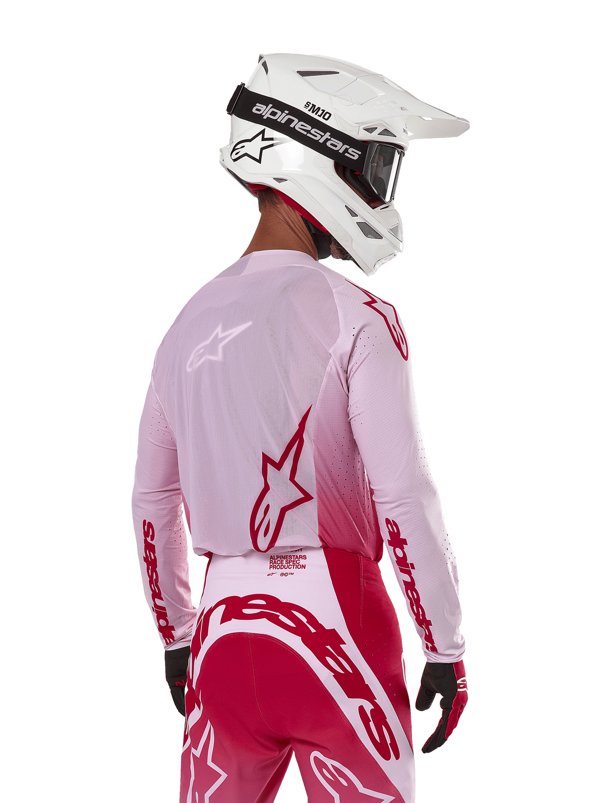 Motocyklista motocrossowy widziany od tyłu w koszulce Alpinestars 2024 Supertech Dade w kolorze Red Berry Lilac, z oddychającymi panelami z siatki i czerwonymi logo Alpinestars, w zestawie z pasującymi czerwono-liliowymi spodniami oraz białym kaskiem Alpinestars z goglami, profesjonalny sprzęt do wyścigów off-road