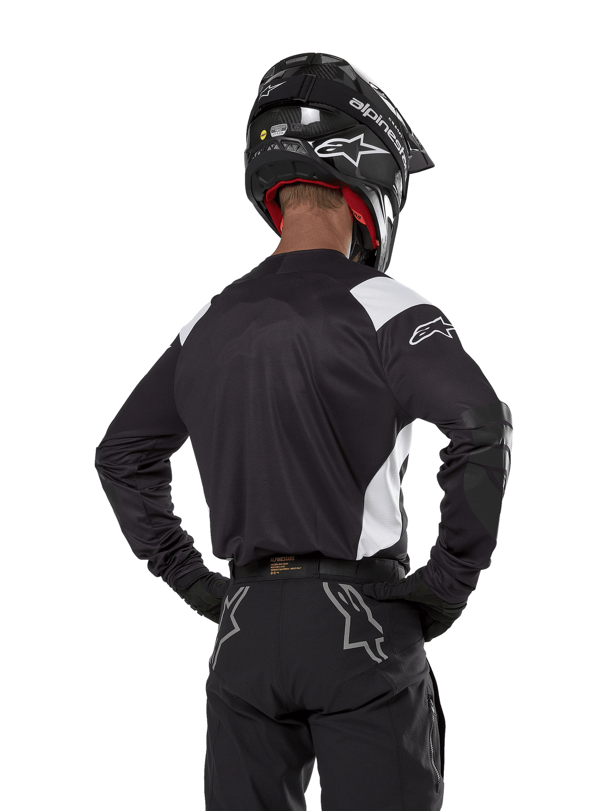 Alpinestars Techdura Jersey, czarna z białymi akcentami na ramionach, widok z tyłu na motocyklistę w pasujących czarnych spodniach i kasku, wzmocnione łaty na łokciach, odzież do enduro i jazdy terenowej