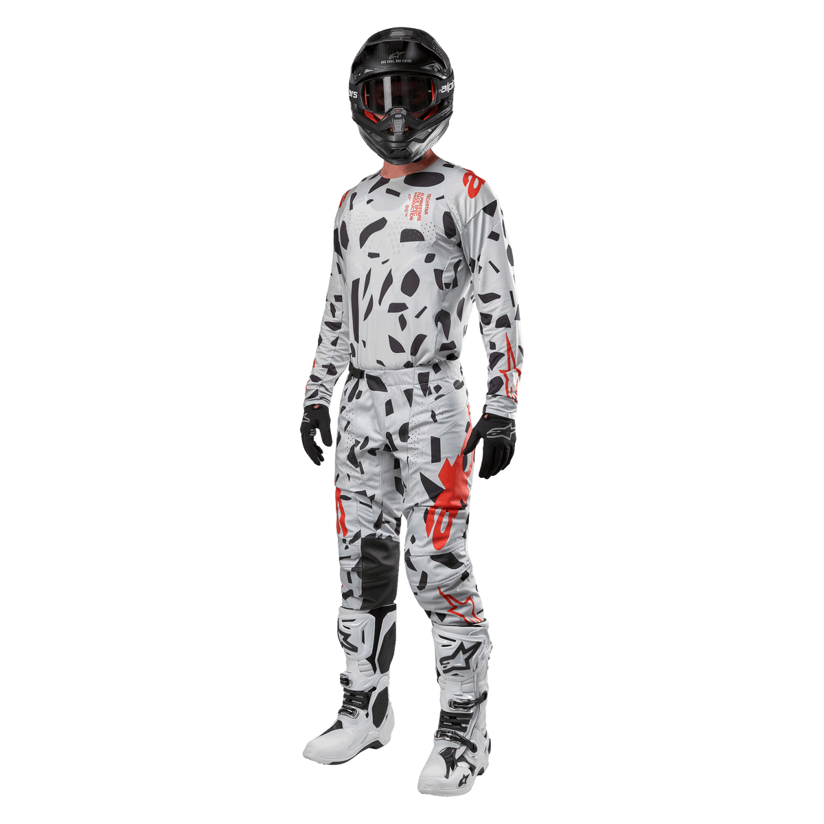 Zawodnik motocrossowy w koszulce Alpinestars 2024 Techstar Rantera w kolorze Haze Gray Camo, pasujące spodnie z czerwonymi i czarnymi akcentami, czarny kask i gogle, czarne rękawice, biało-czarne buty, kompletny, skoordynowany zestaw wyścigowy motocross do jazdy terenowej