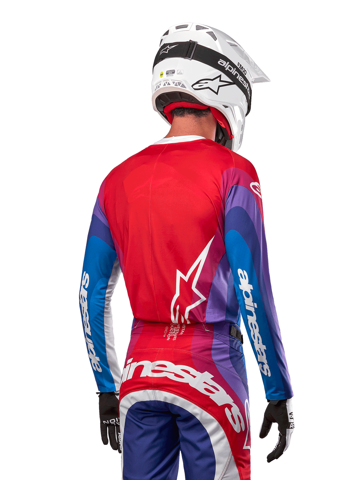 Zawodnik motocrossowy od tyłu w koszulce Alpinestars 2024 Techstar Pneuma w kolorze Blue Mars Red White, czerwony tył z białym logo gwiazdy, niebieskie i fioletowe rękawy z białym brandingiem, w komplecie z pasującymi spodniami i białym kaskiem do jazdy terenowej.