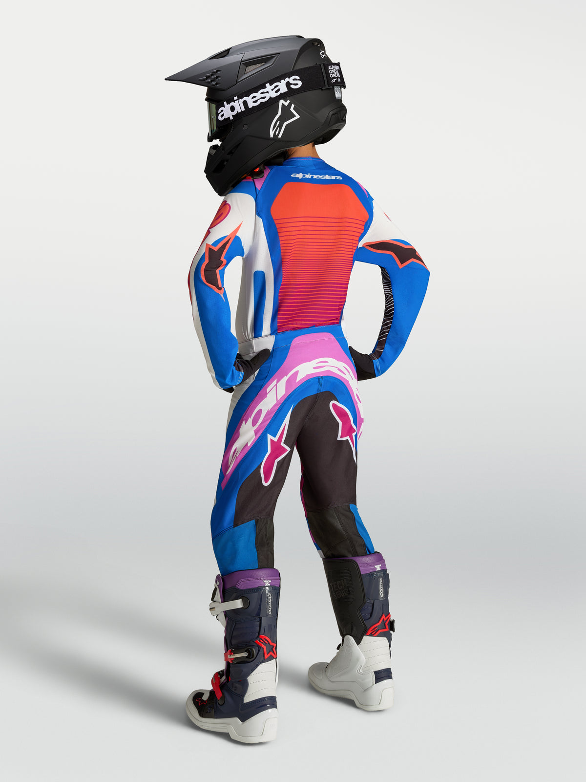 Alpinestars Młodzieżowy Zestaw Supertech Maven 2027, niebiesko-koralowy strój motocrossowy, widok z tyłu na zawodniku.