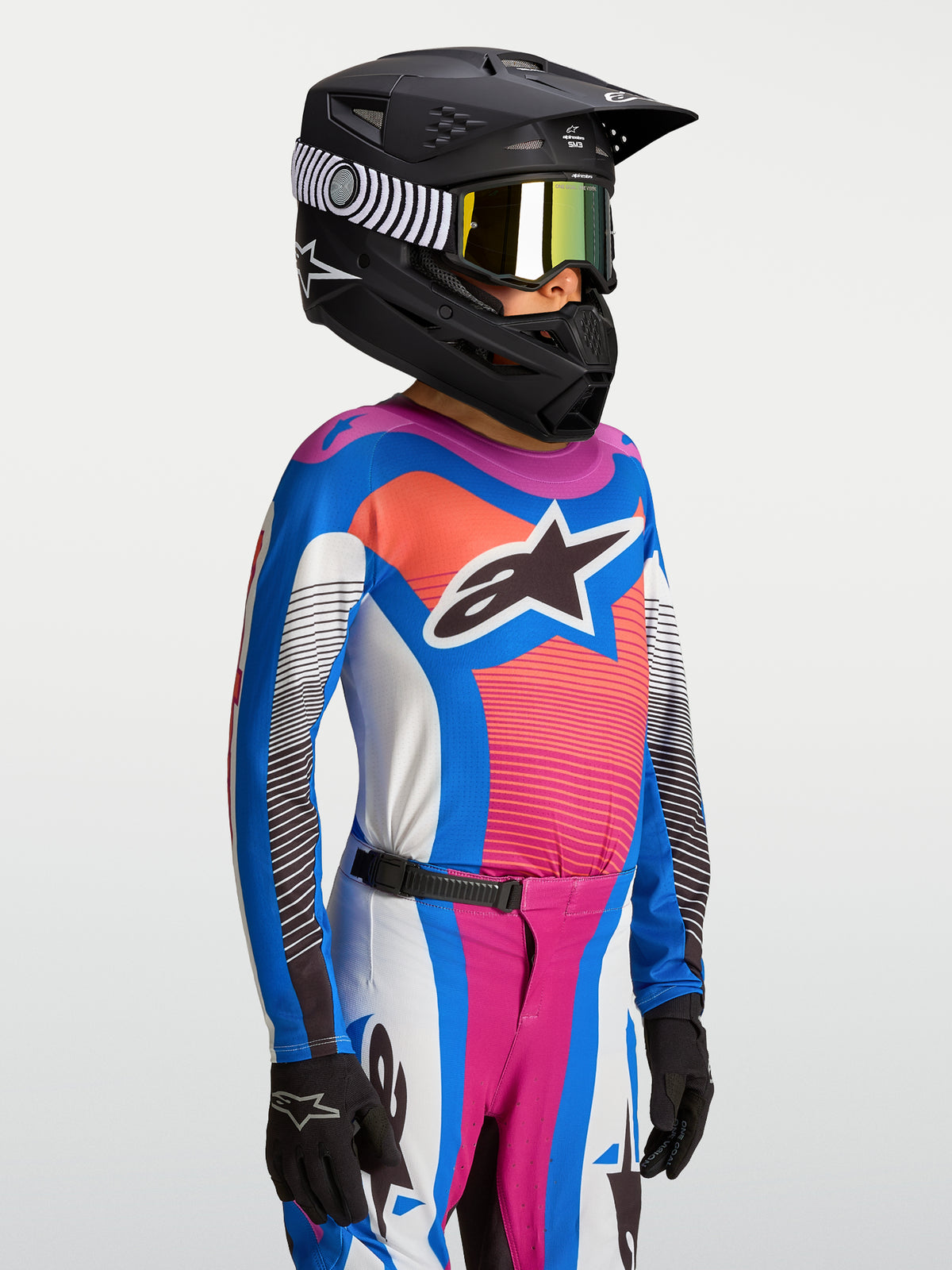Alpinestars Supertech Maven, koszulka młodzieżowa, niebieska i koralowa odzież MX, czarny kask wyścigowy.