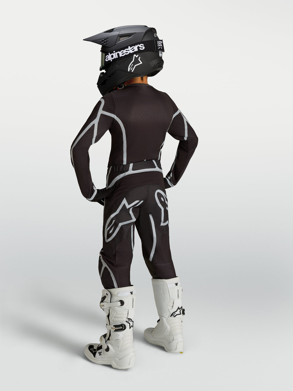 Alpinestars 2027 Youth Fluid Apex V2 black and silver motocross gear set, shown in a rear view with white boots.