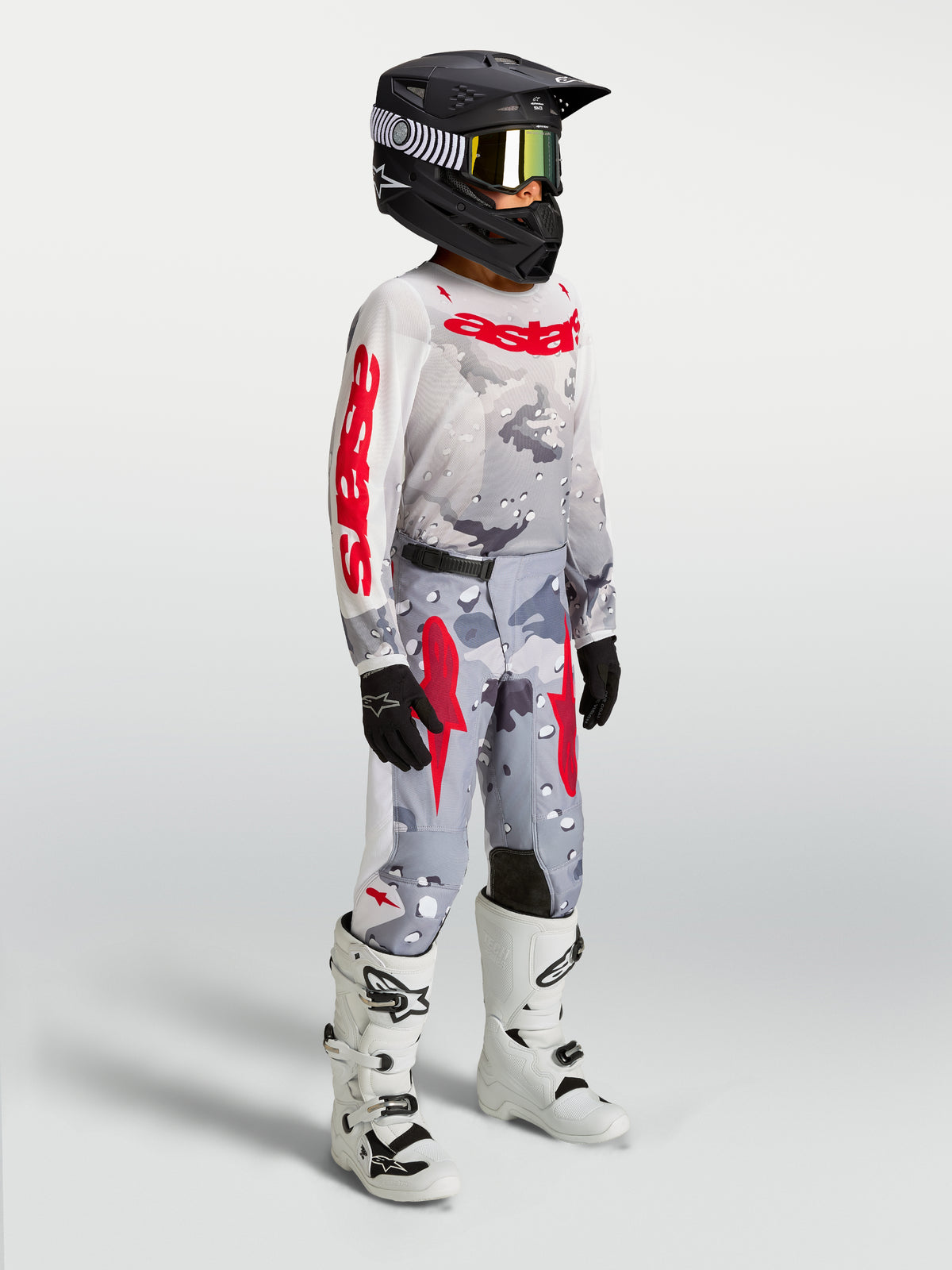 Alpinestars Fluid Lone, młodzieżowy zestaw MX, szary kamuflaż i czerwień, zawodnik w kasku i białych butach.