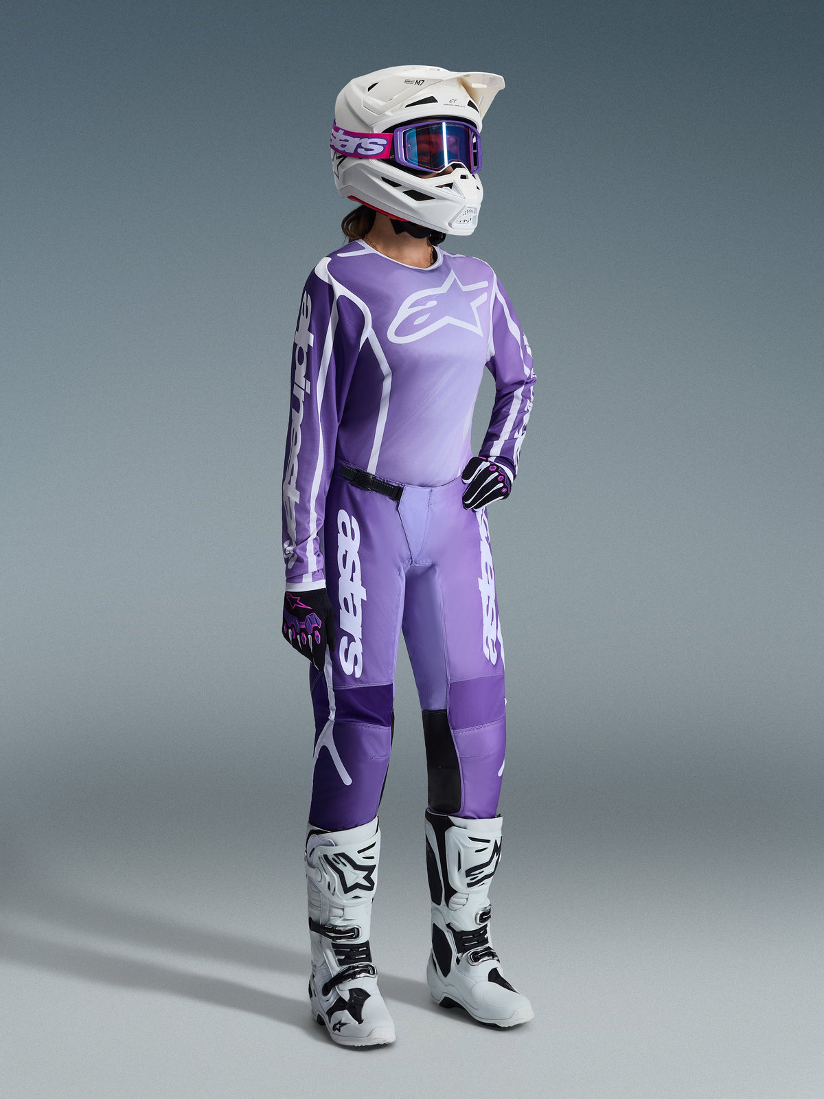 Alpinestars 2026 Stella Fluid Apex Gear Set, fioletowy i lawendowy, motocyklistka motocrossowa w pasującej koszulce i spodniach, biały kask z fioletowymi goglami, biało-czarne buty, czarno-fioletowe rękawice, kompletny strój wyczynowy do kobiecych wyścigów off-road
