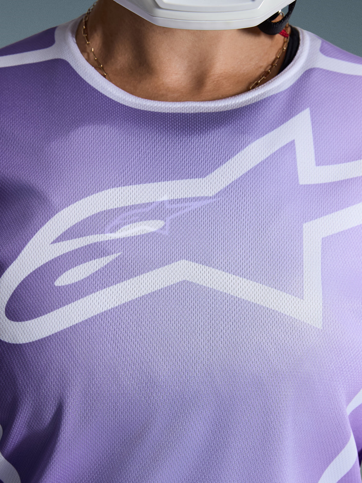 Koszulka Alpinestars Stella Fluid Apex 2026, zbliżenie na klatkę piersiową, fioletowa z białymi grafikami, duże białe logo Astars na siatkowej konstrukcji z poliestru