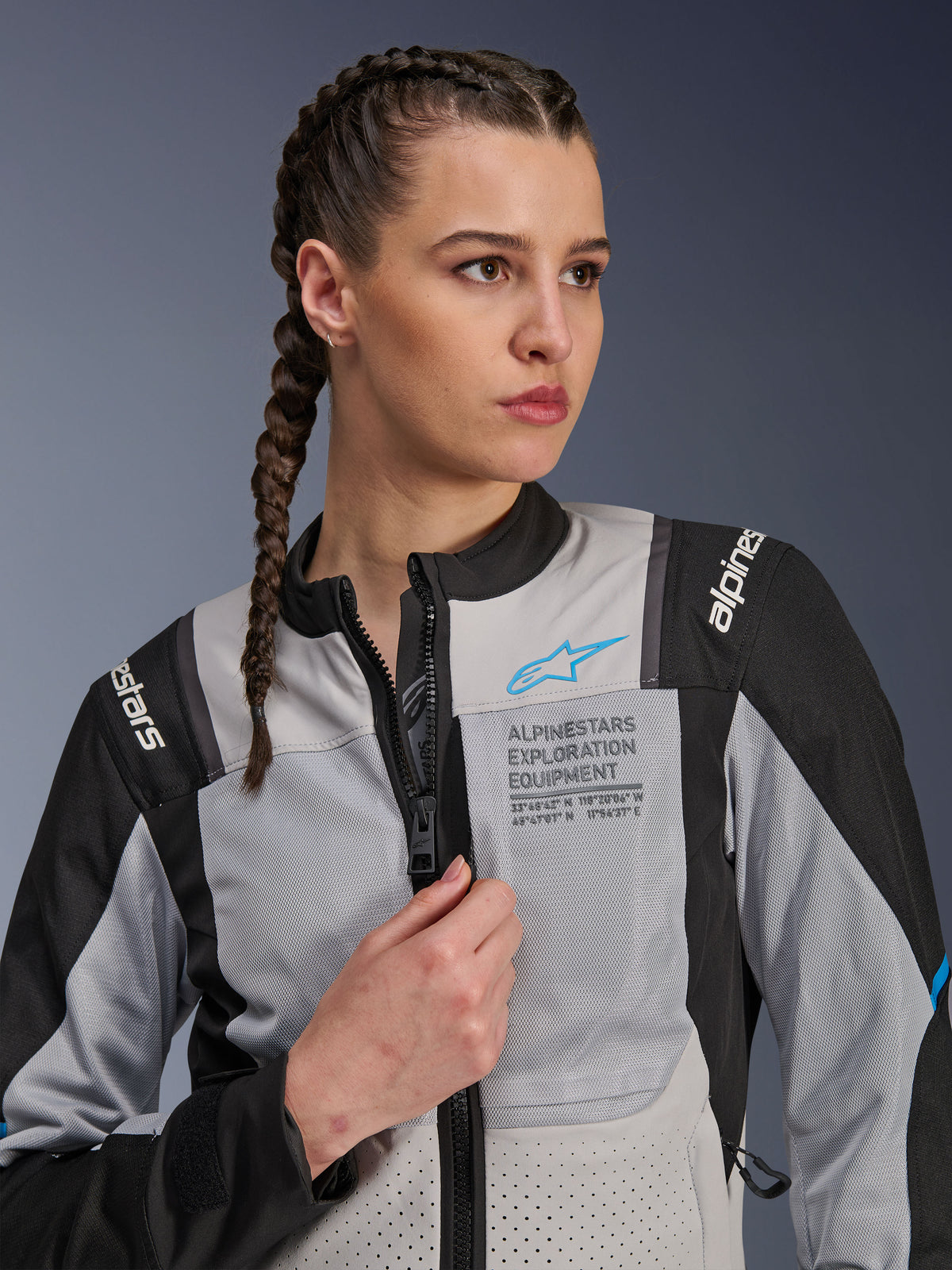 Kobieta w kurtce Alpinestars Stella ST-2 Air w kolorze Ice Gray i czarnym, portret z bliska, siatkowe panele wentylacyjne, branding „ALPINESTARS EXPLORATION EQUIPMENT” na klatce piersiowej z niebieskim logo, nowoczesna motocyklowa kurtka adventure