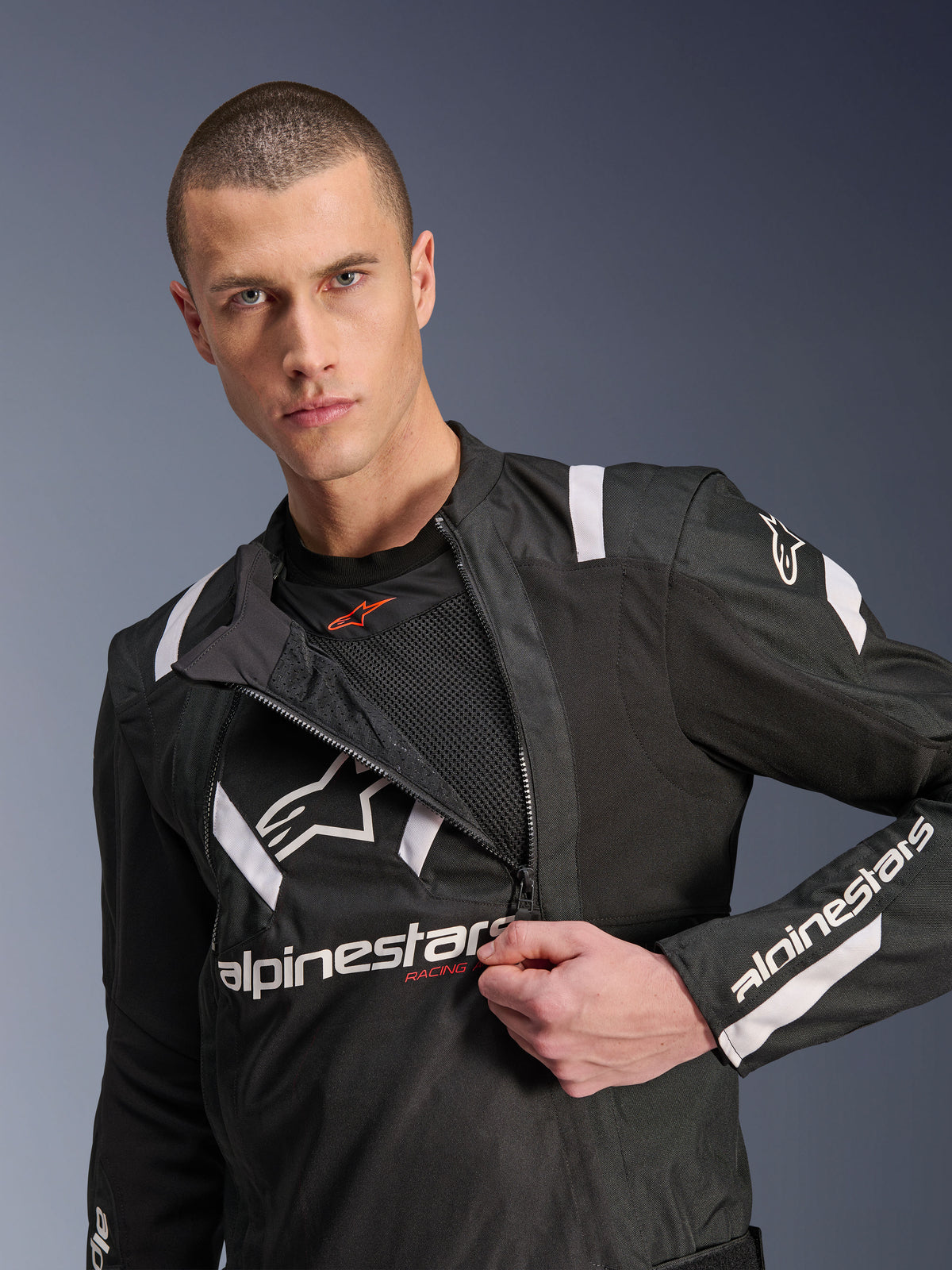 Alpinestars T-Stunt Air Jacket, czarno-biała kurtka motocyklowa, model prezentujący częściowo rozpięty modułowy panel przedni odsłaniający siatkowe warstwy wentylacyjne, białe logo Alpinestars na klatce piersiowej i rękawach, sportowy design do jazdy szosowej