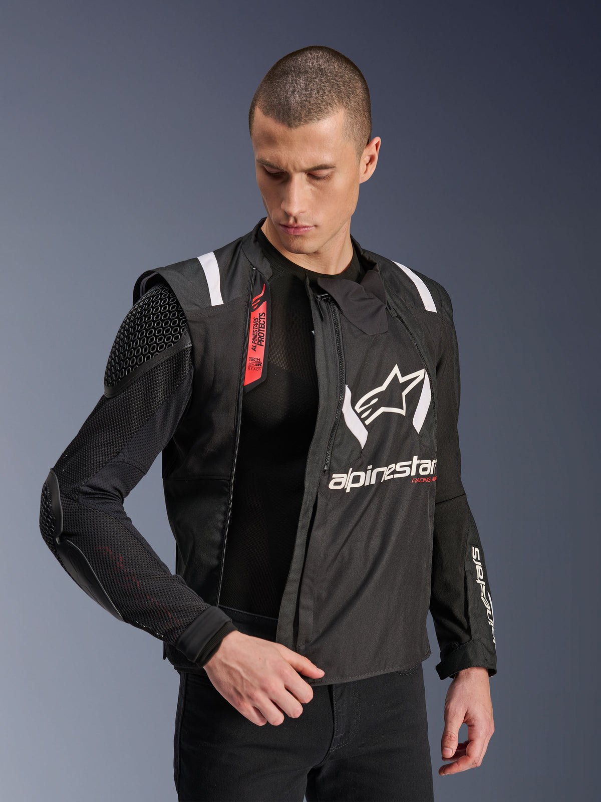 Kurtka motocyklowa Alpinestars T-Stunt Air Jacket, czarno-biała, noszona przez modela, prezentująca modułową konstrukcję z siatki i widoczne wewnętrzne ochraniacze na ramieniu i łokciu, logo Alpinestars na klatce piersiowej, system Tech-Air Ready, sportowy krój do jazdy szosowej