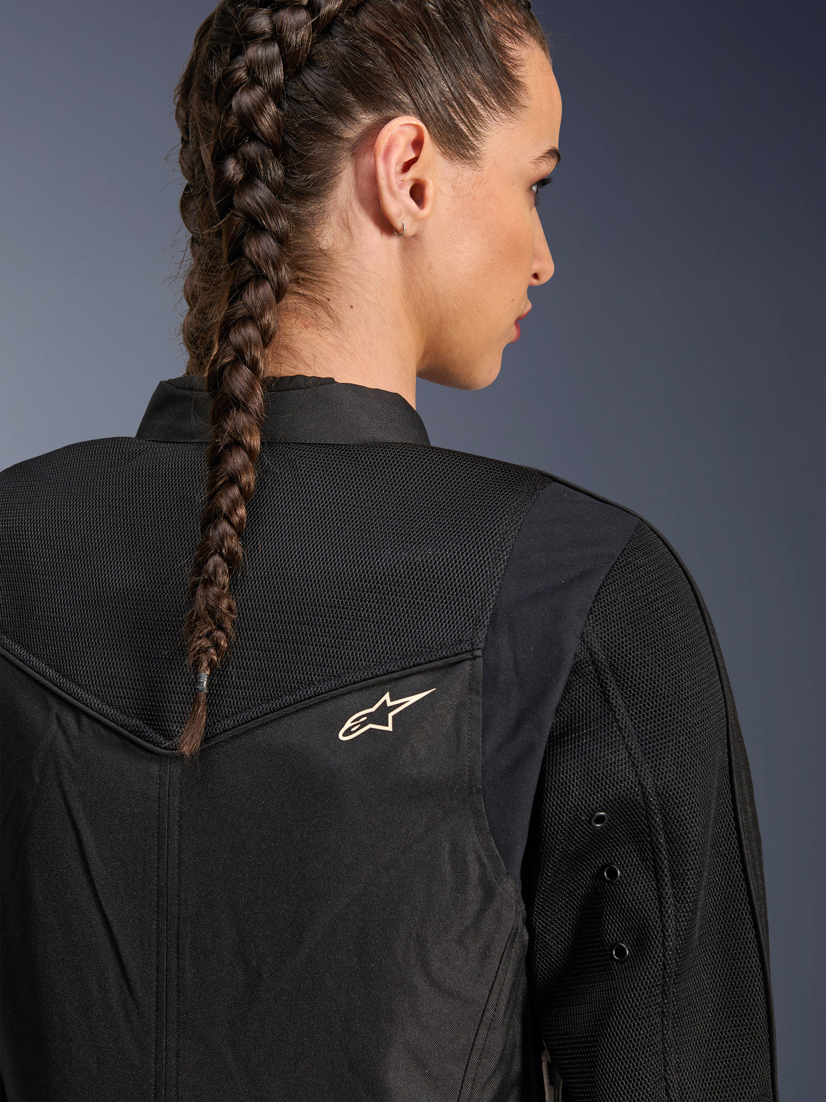 Alpinestars Stella T-Dyno Air Jacket, damska czarna kurtka motocyklowa, zbliżenie na tył pokazujące panele z siatki 3D na karczku i górnej części pleców dla przepływu powietrza, małe białe logo gwiazdy, modelka z warkoczem