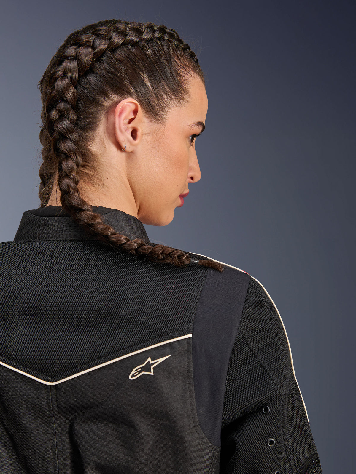 Kobieta w kurtce Alpinestars Stella T-Dyno Air, zbliżenie z tyłu na ramiona i karczek, czarna z oddychającymi panelami z siatki 3D, białe lamówki i małe logo Astars, modelka z zaplecionymi włosami, miejska odzież motocyklowa