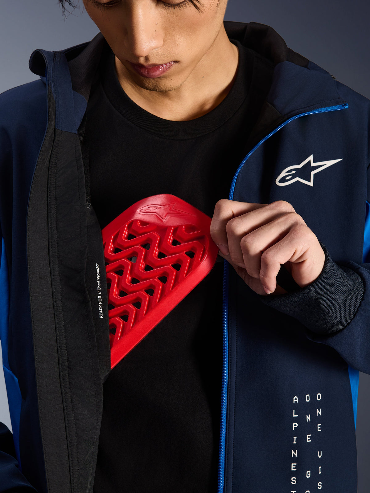 Alpinestars Radium Tech Hoodie w kolorach Night Navy i Royal Blue, zbliżenie pokazujące czerwony ochraniacz klatki piersiowej Nucleon wkładany do wewnętrznej kieszeni, z napisem „READY FOR // Chest Protector” na podszewce i białym logo gwiazdy na klatce piersiowej.