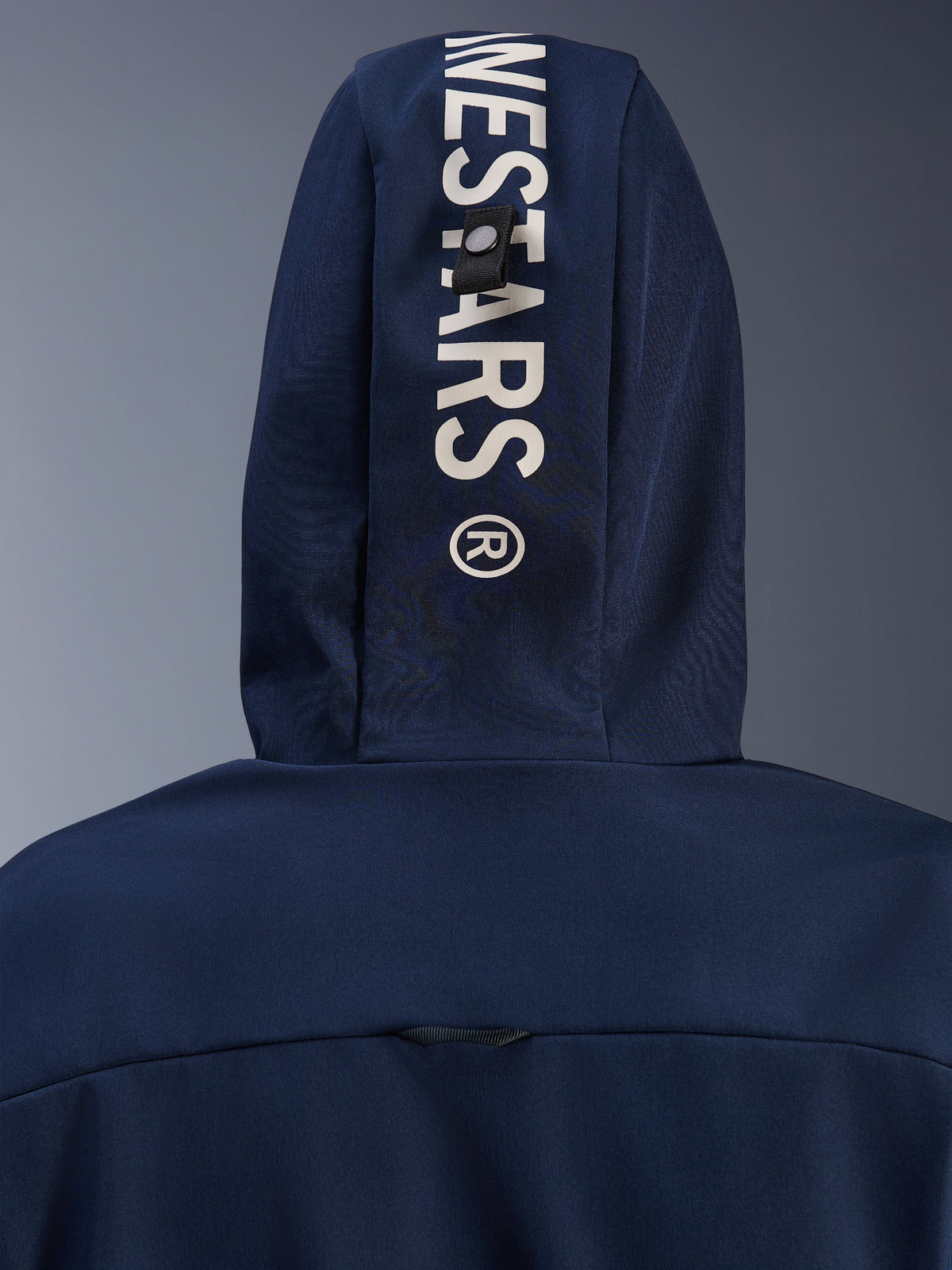 Alpinestars Radium Tech Hoodie w kolorze Night Navy Royal Blue, zbliżenie na tył kaptura z pionowym białym brandingiem Alpinestars i systemem mocowania na pętlę, miejska techniczna odzież motocyklowa
