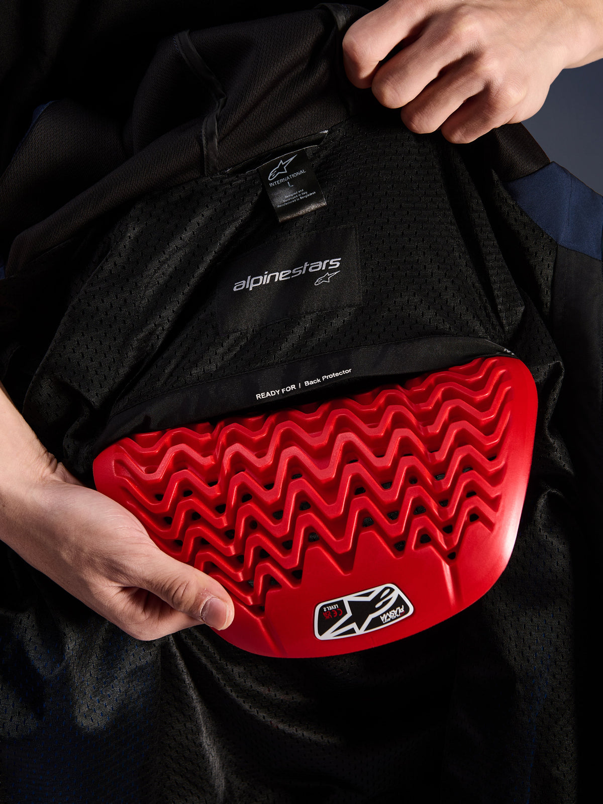 Alpinestars Radium Tech Hoodie, detal wnętrza, czerwony ochraniacz pleców Nucleon Plasma wkładany do kieszeni na ochraniacz, czarna podszewka mesh z napisem 'READY FOR | Back Protector', falista struktura plastra miodu, techniczne elementy ochronne miejskiej kurtki motocyklowej