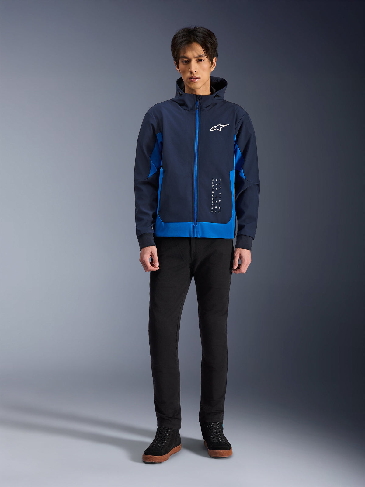 Alpinestars Radium Tech Hoodie, miejska bluza motocyklowa w kolorach Night Navy i Royal Blue, wiatroszczelna powłoka techniczna, casualowy design streetwearowy, zestawiona z czarnymi spodniami i wysokimi sneakersami, białe logo na piersi