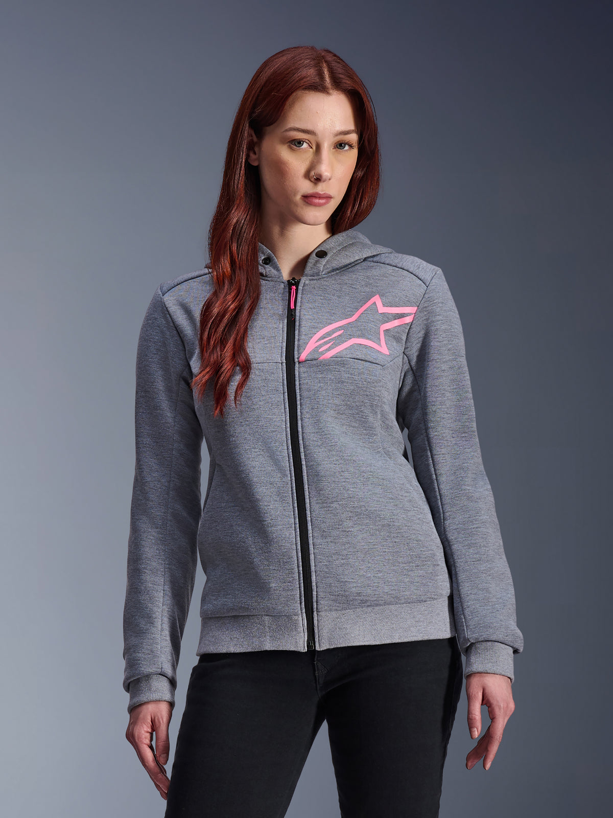 Alpinestars Stella Chrome V2 Sport Hoodie, damska motocyklowa bluza z kapturem, szary melanż z różowym logo gwiazdy fluo, techniczny polar ze ściągaczami na mankietach i na dole, czarny przedni suwak z różowym uchwytem, miejska odzież motocyklowa noszona z czarnymi spodniami