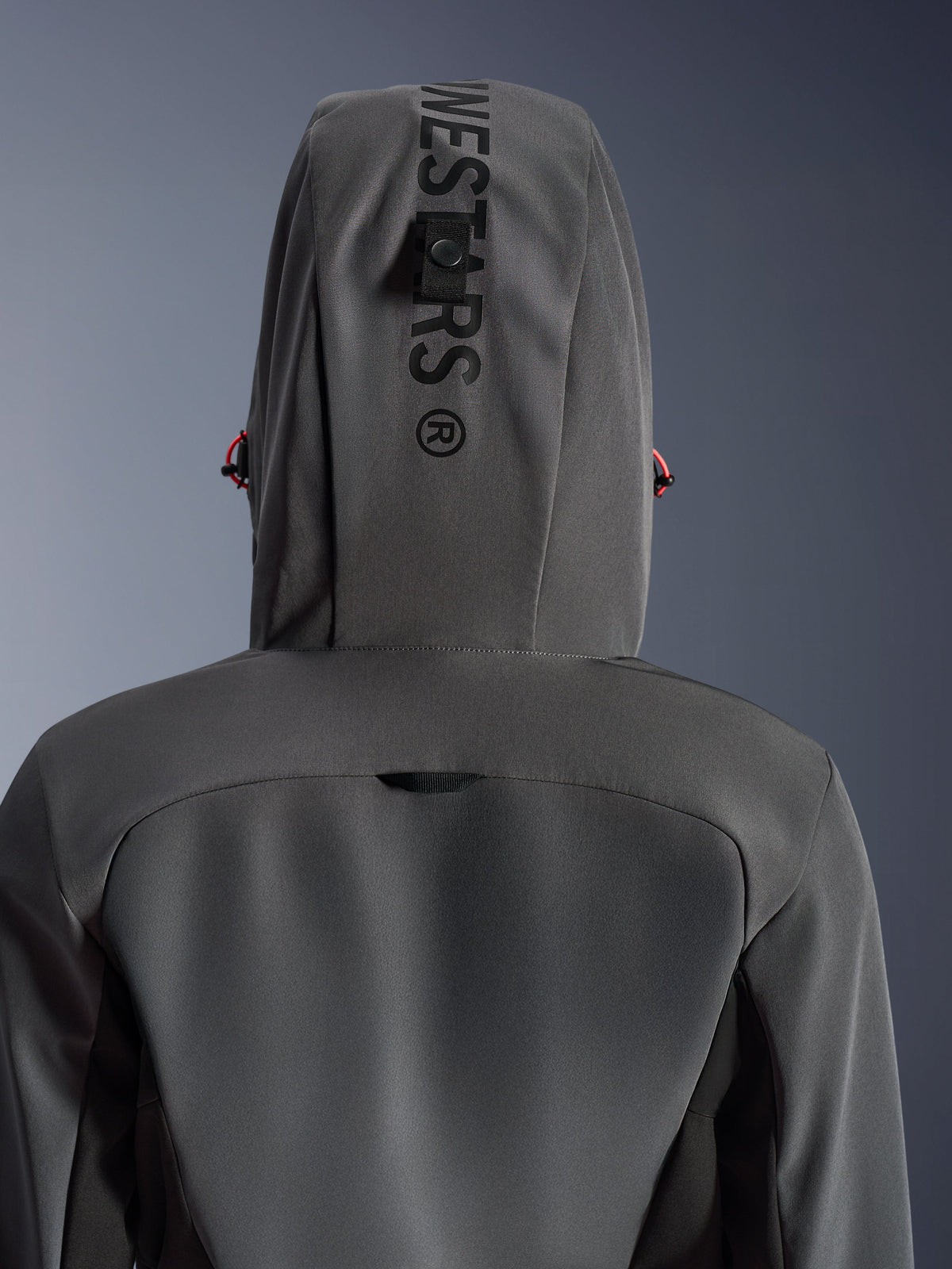 Alpinestars Woman Stella Radium Tech Hoodie, kolor Deep Gray Black, zbliżenie na tył pokazujące kaptur z pionowym brandingiem i pętlą mocującą, czerwone akcenty ściągaczy, wytrzymała 3-warstwowa wiatroszczelna konstrukcja tekstylna do jazdy miejskiej.
