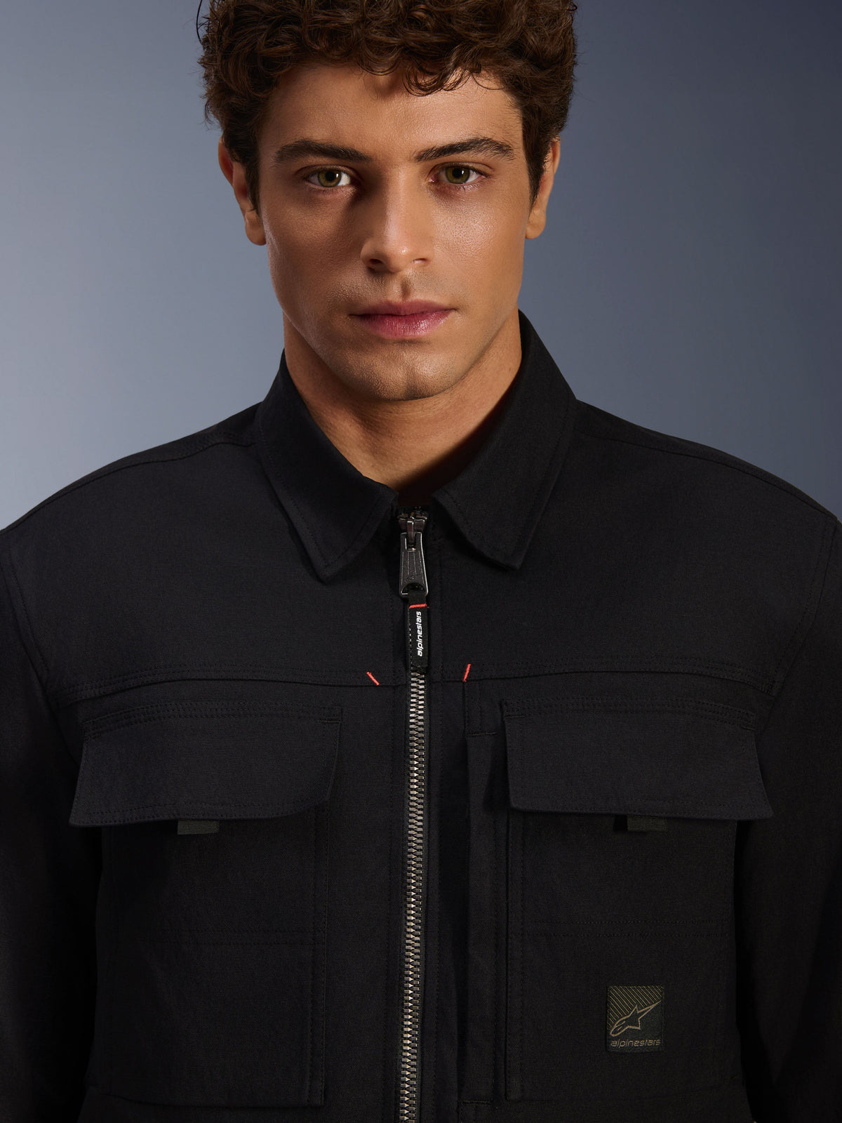 Alpinestars Bryon Water Resistant Overshirt, czarna, zbliżenie na przedni zamek i kieszenie na piersi, wytrzymała tekstura woskowanego płótna, minimalistyczny miejski design z markowymi akcentami i tkaną metką z logo
