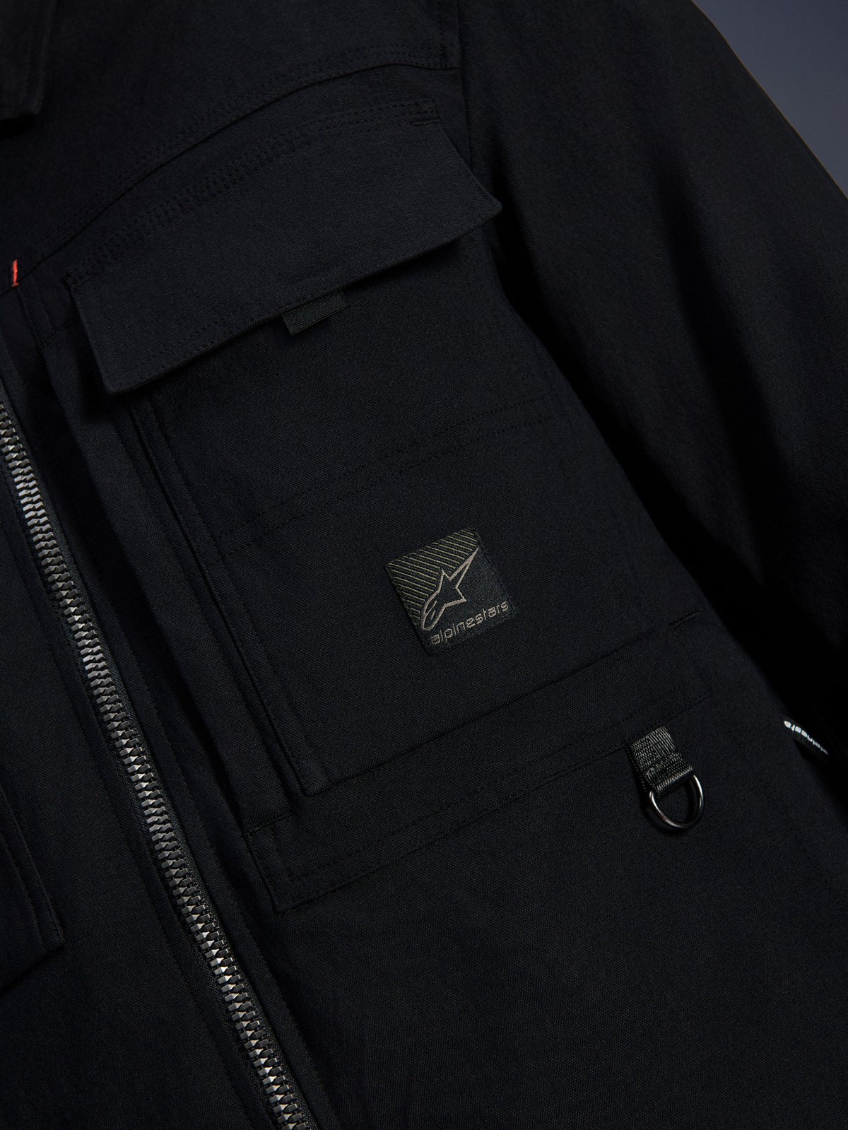 Alpinestars Bryon Water Resistant Overshirt, czarna, zbliżenie na woskowane płótno, przedni zamek błyskawiczny, kieszeń cargo na piersi z naszywką z logo Alpinestars i metalowy detal D-ring