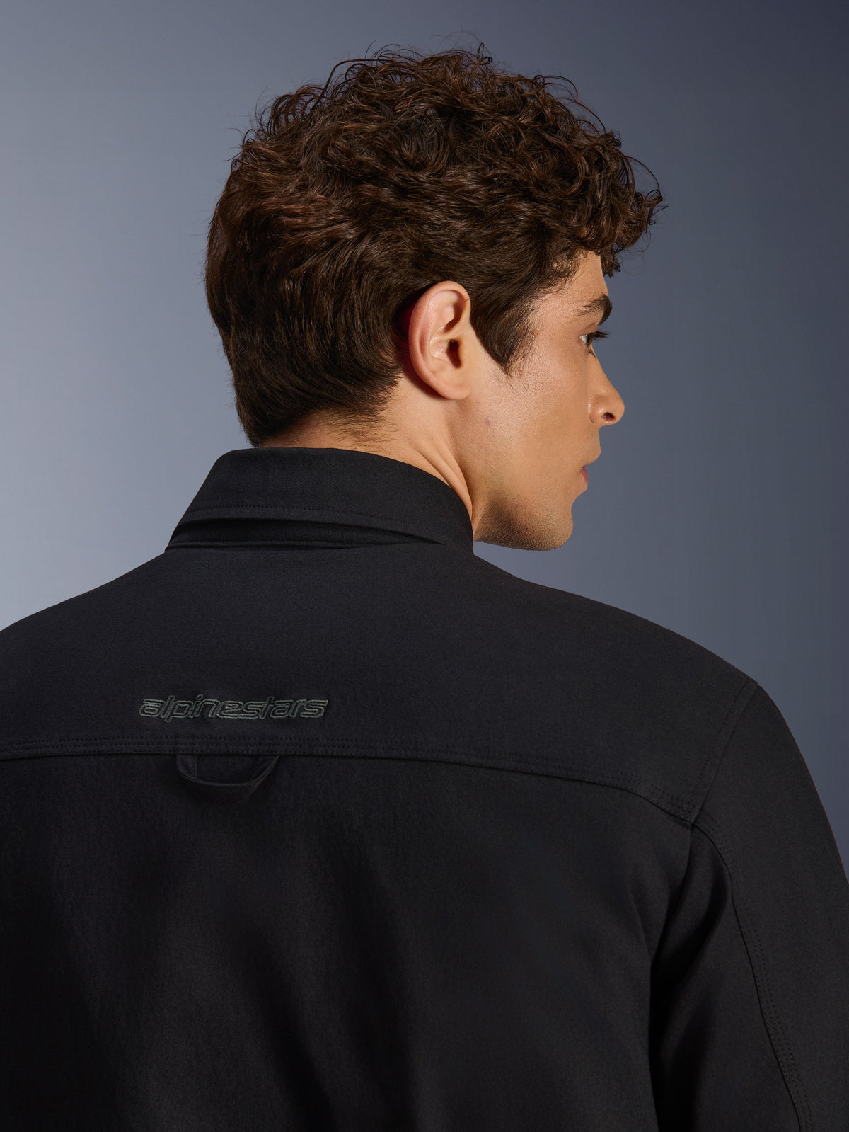 Alpinestars Bryon Water Resistant Overshirt, miejska kurtka motocyklowa, czarna, zbliżenie na tylną część ramion z haftowanym logo i pętlą do zawieszania, wodoodporna konstrukcja z woskowanego płótna.