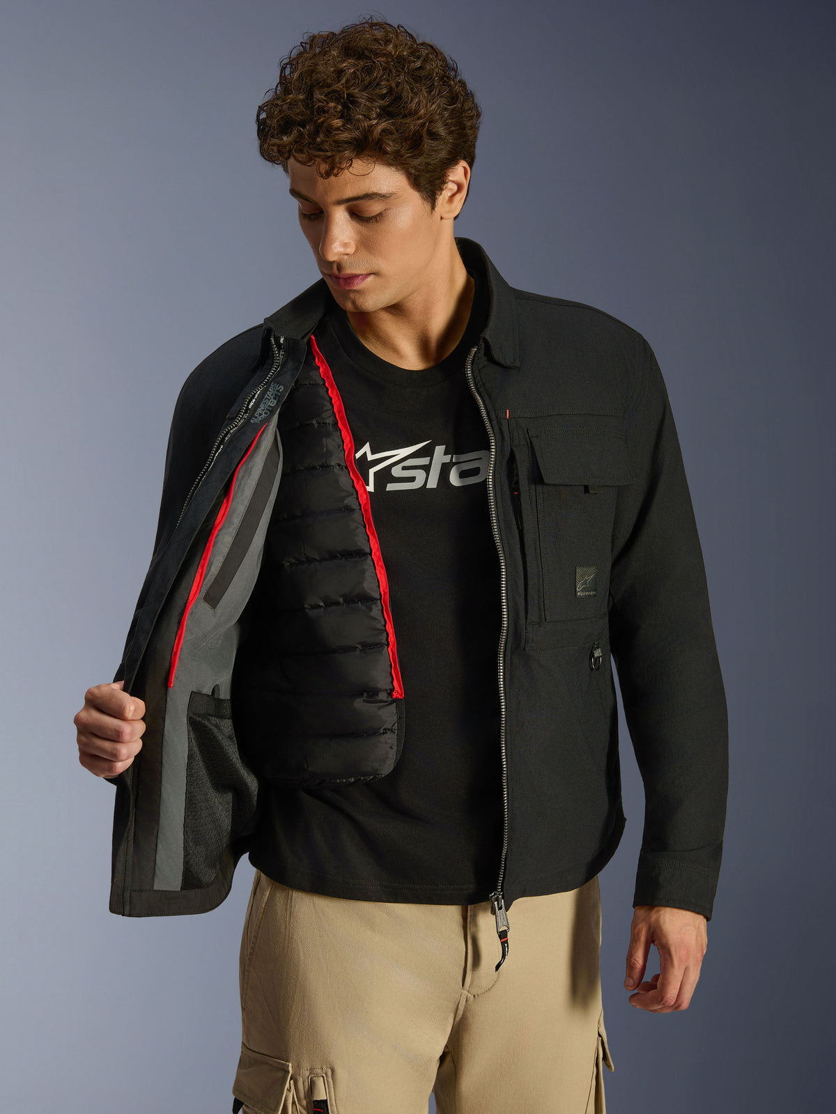 Alpinestars Bryon WR Overshirt, czarna miejska kurtka motocyklowa, rozpięta, odsłaniająca odpinaną czarną pikowaną kamizelkę termiczną z czerwonym wykończeniem, noszona z beżowymi spodniami cargo i koszulką z logo, funkcjonalny design inspirowany odzieżą roboczą