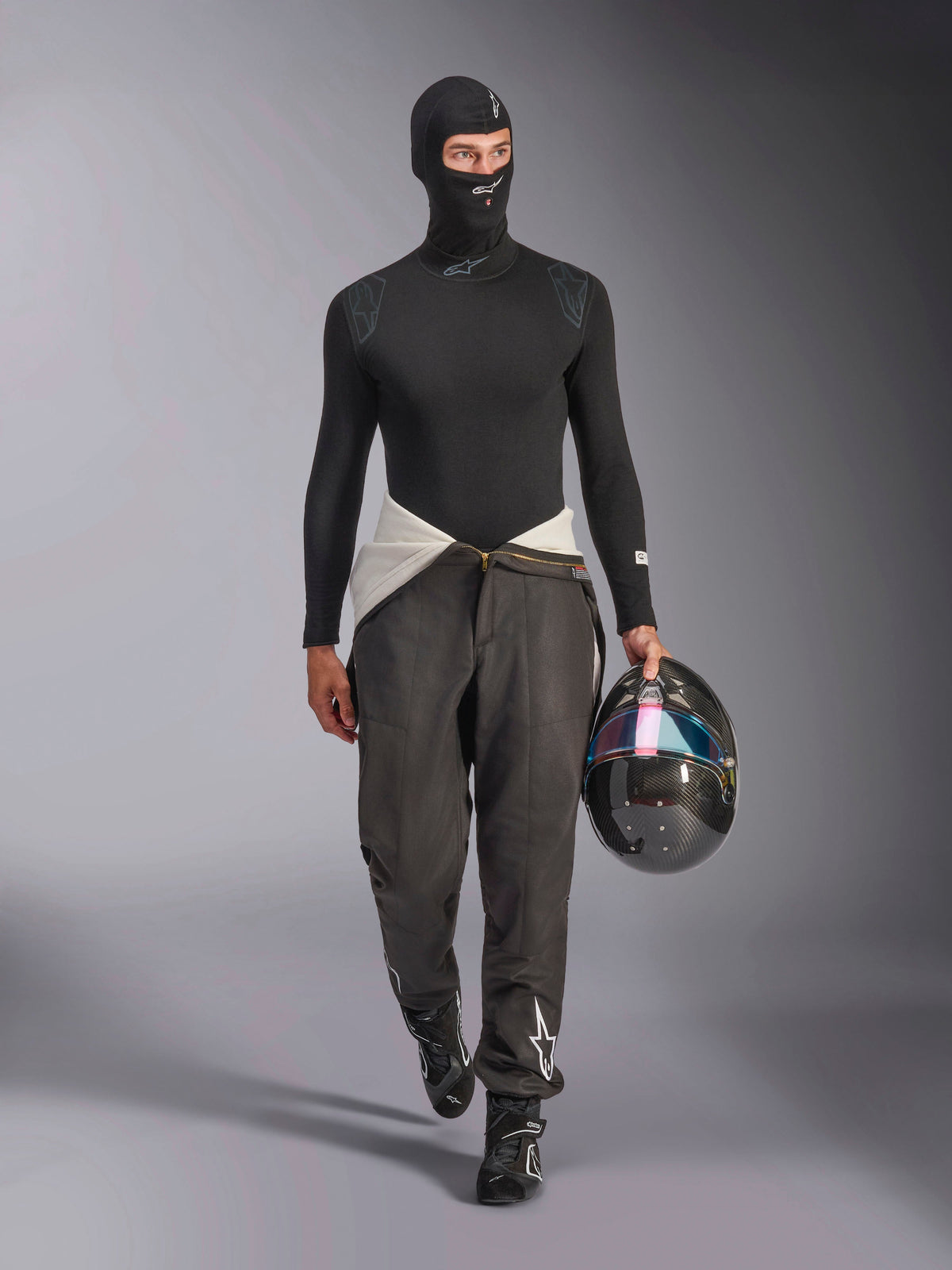 Kominiarka Alpinestars ZX Evo V3, czarna, model w pełnym stroju wyścigowym typu base layer z koszulką z długim rękawem i szarymi spodniami, kask z włókna węglowego z opalizującym wizjerem, profesjonalny sprzęt do wyścigów samochodowych