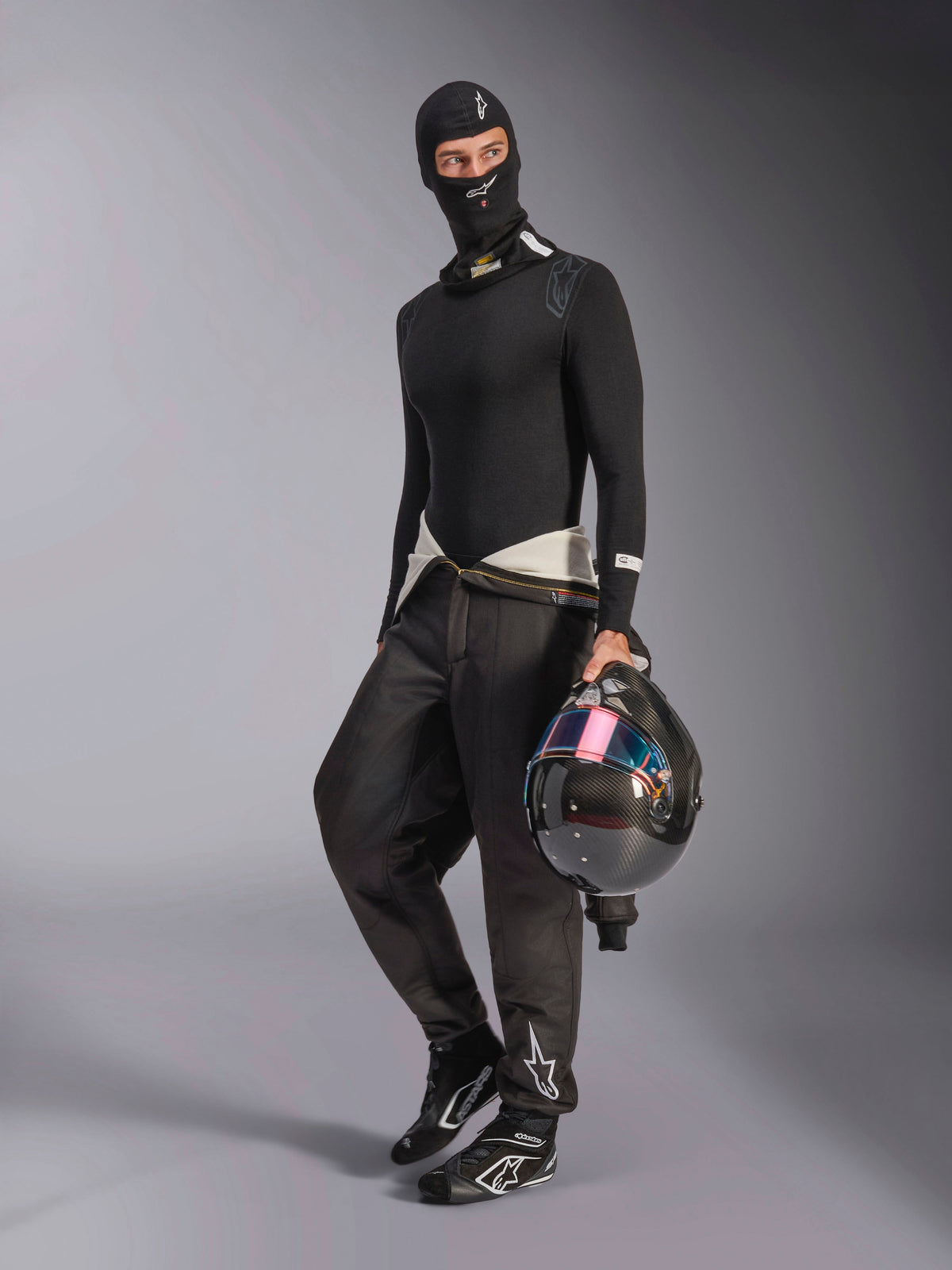 Alpinestars ZX Evo V3 Balaclava, czarna kominiarka noszona przez kierowcę w pełnym zestawie samochodowej bielizny termoaktywnej, białe logo na czole, kask z włókna węglowego z opalizującym wizjerem, profesjonalna ognioodporna odzież motorsportowa