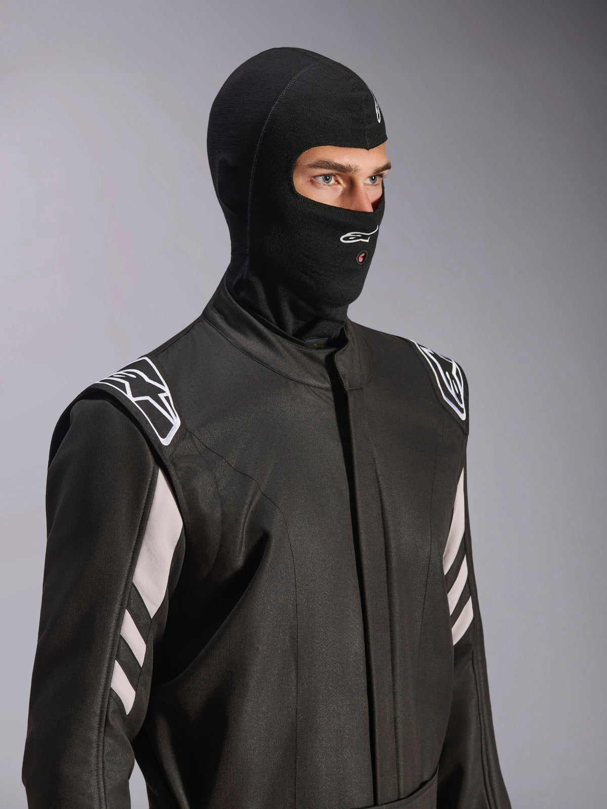 Kominiarka Alpinestars ZX Evo V3, czarna, ognioodporna kominiarka wyścigowa, noszona przez modela w czarnym kombinezonie z białymi akcentami, logo Alpinestars na podbródku, otwór na rurkę nawadniającą, profesjonalny sprzęt ochronny do sportów motorowych