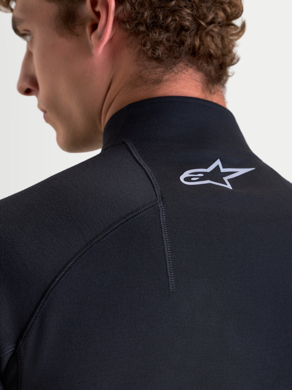 Alpinestars AT-8 Merino Top, męski top z bielizny technicznej motocyklowej w kolorze czarnym, zbliżenie na model prezentujące konstrukcję rękawów raglanowych, wyprofilowany kołnierz oraz szczegół białego logo Alpinestars z tyłu