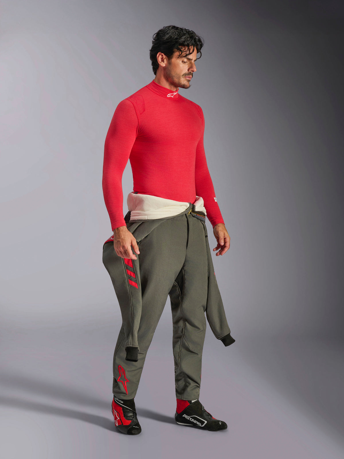 Alpinestars ZX Evo V3 Long Sleeve Top in Red, fire-resistant auto racing base layer, worn with olive green racing trousers and black and red racing shoes, professional motorsport gear, studio portrait