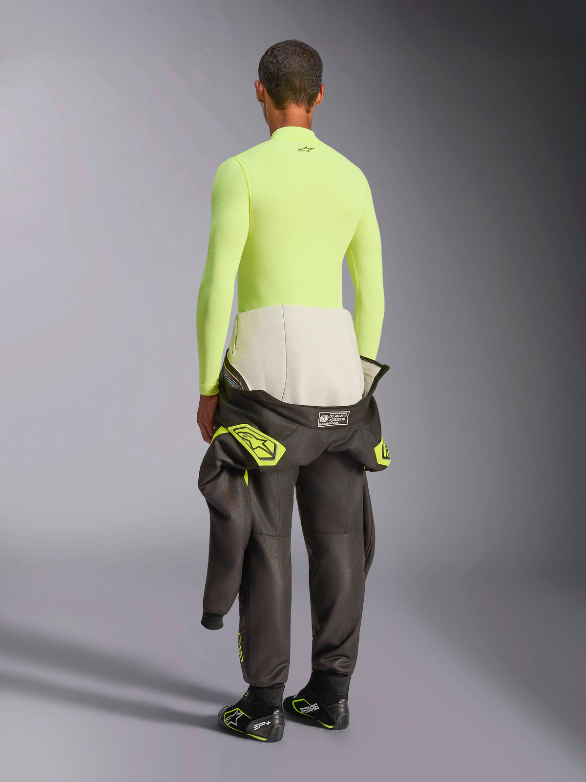 Alpinestars ZX Evo V3 Top - Długi Rękaw, Yellow Fluo, widok z tyłu na modela w ognioodpornej warstwie bazowej, ciemne spodnie od kombinezonu wyścigowego i buty, profesjonalna techniczna bielizna motorsportowa