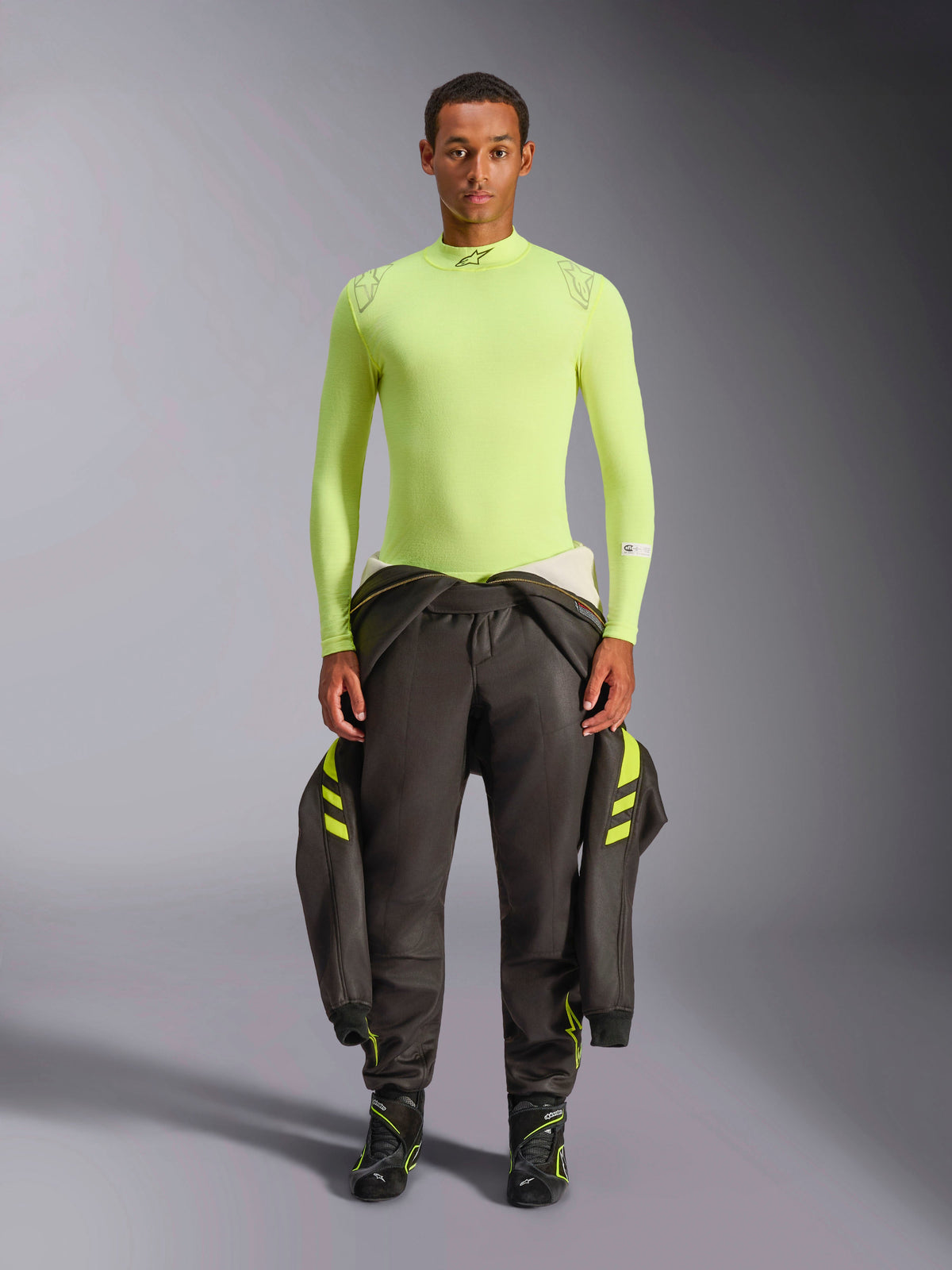 Alpinestars ZX Evo V3 Top - Long Sleeve, kolor żółty neonowy, prezentowany na modelu w ciemnych spodniach wyścigowych i butach, sportowy krój ze stójką, ognioodporna bielizna termoaktywna do profesjonalnych wyścigów samochodowych